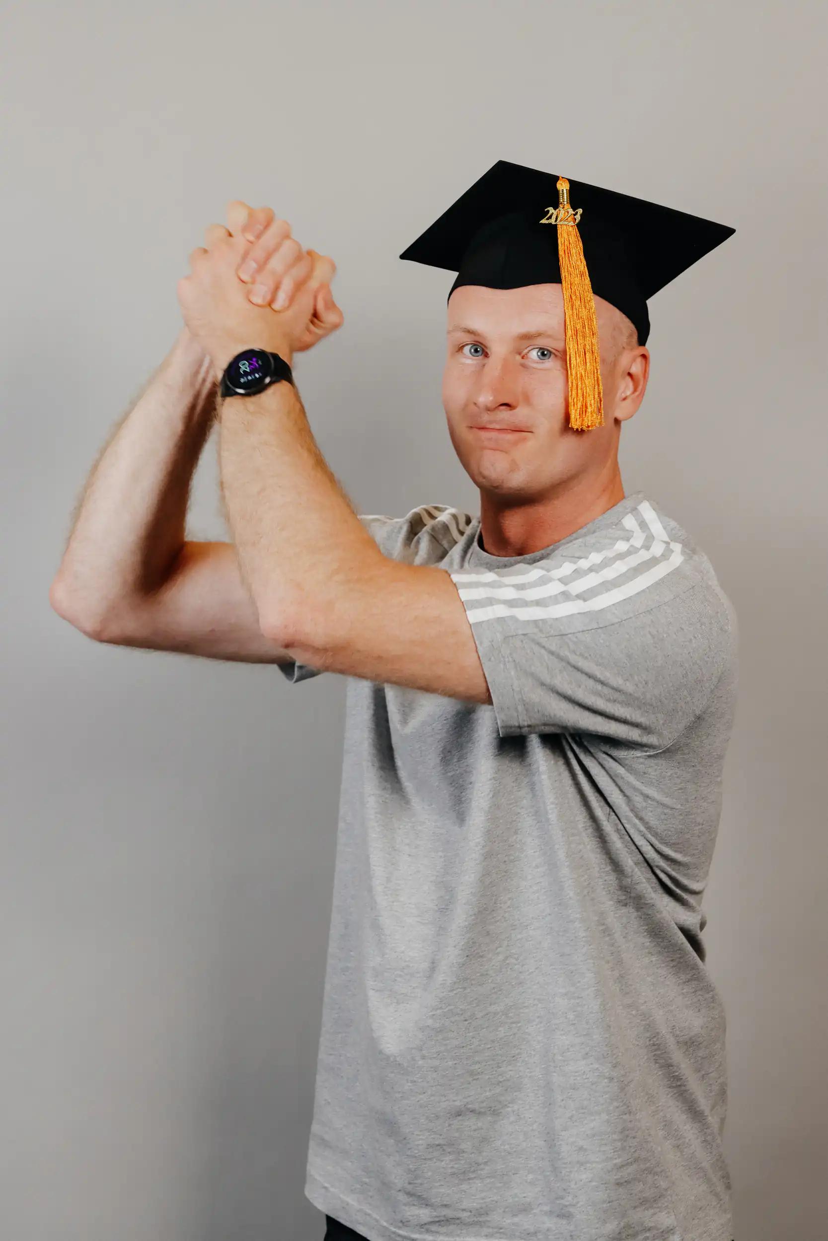 Man wearing a gray shirt and a black graduation cap with tassel posing.