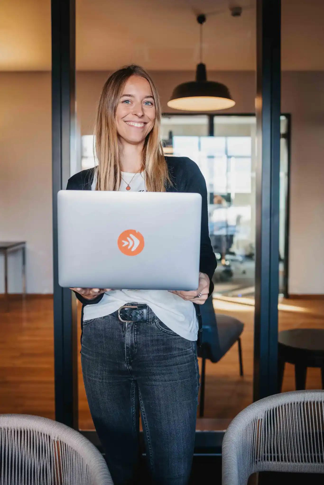 Woman holding a laptop and smiling in an office.