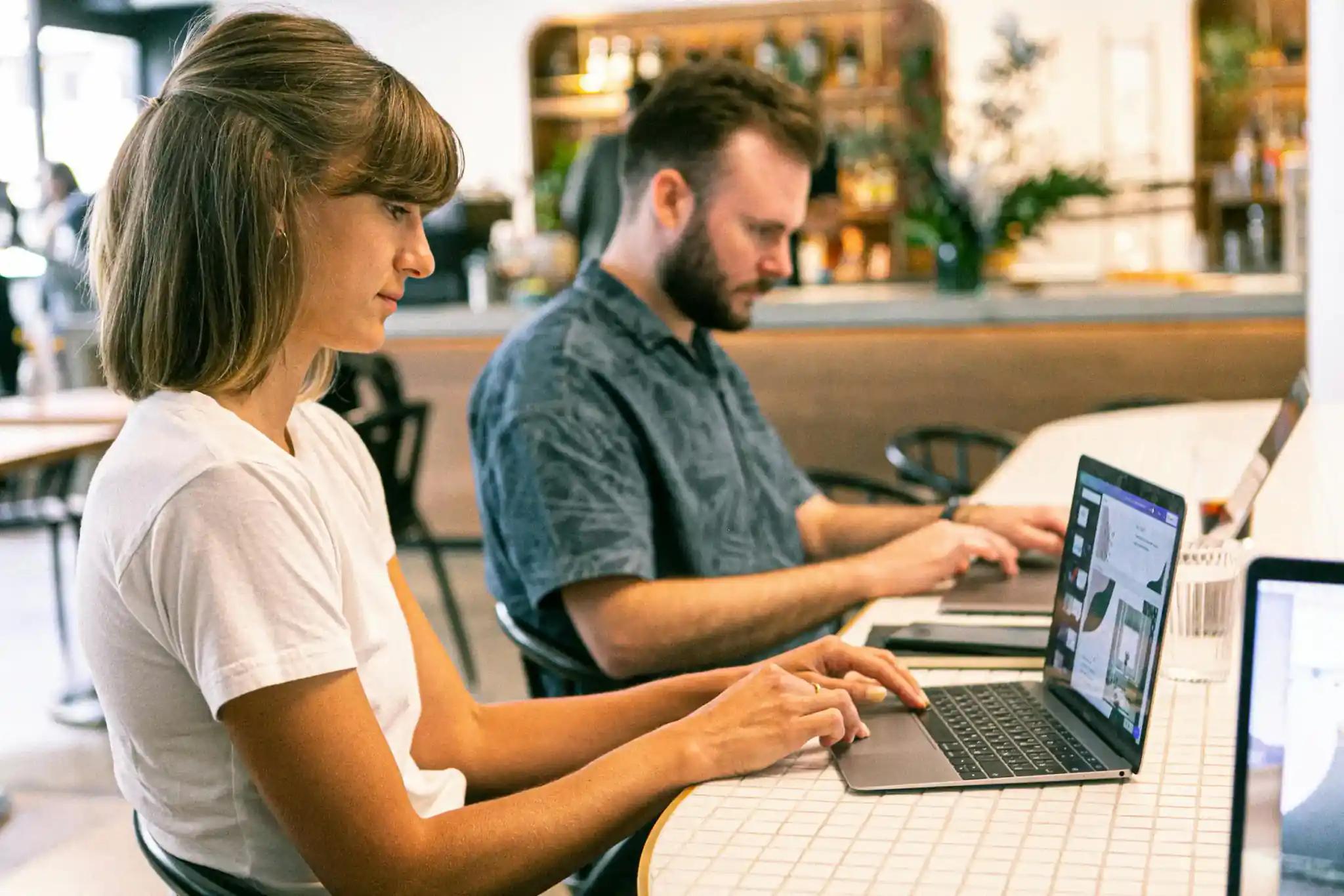 Two people working on laptops in a café.