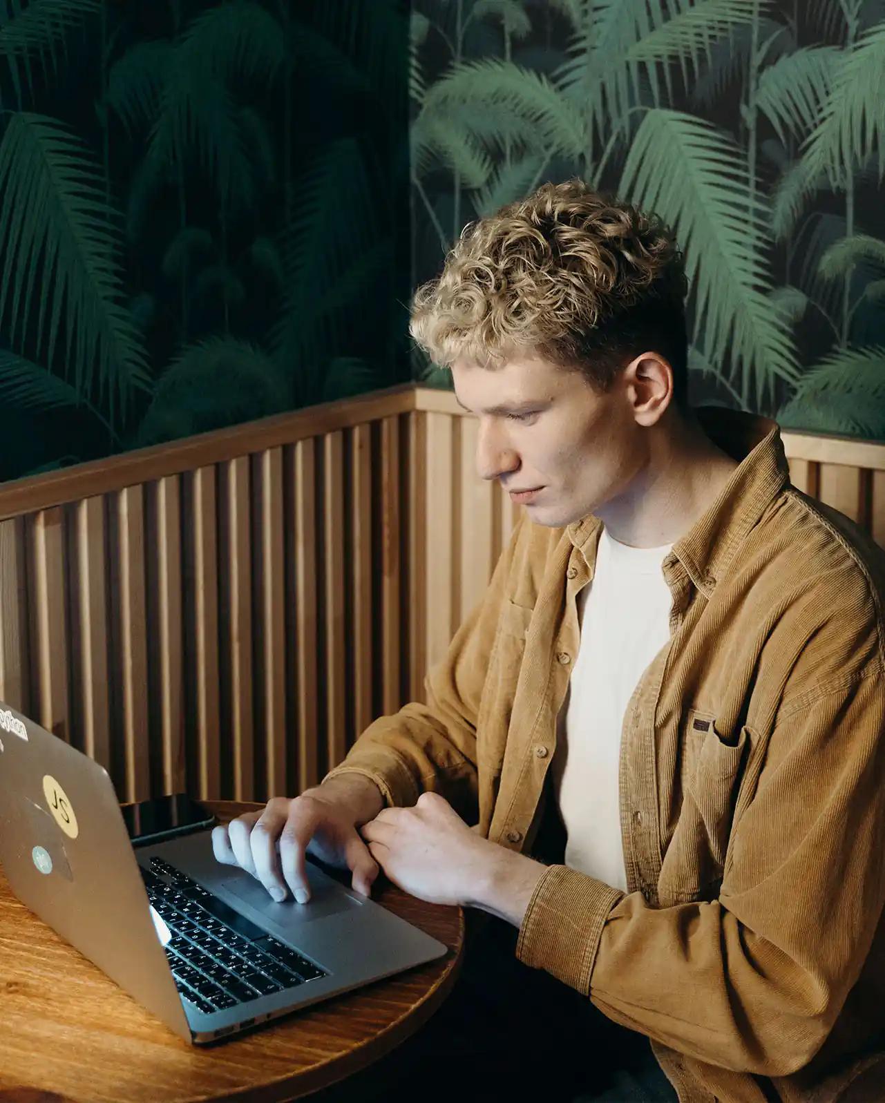 Junger Mann, der an einem Laptop arbeitet.