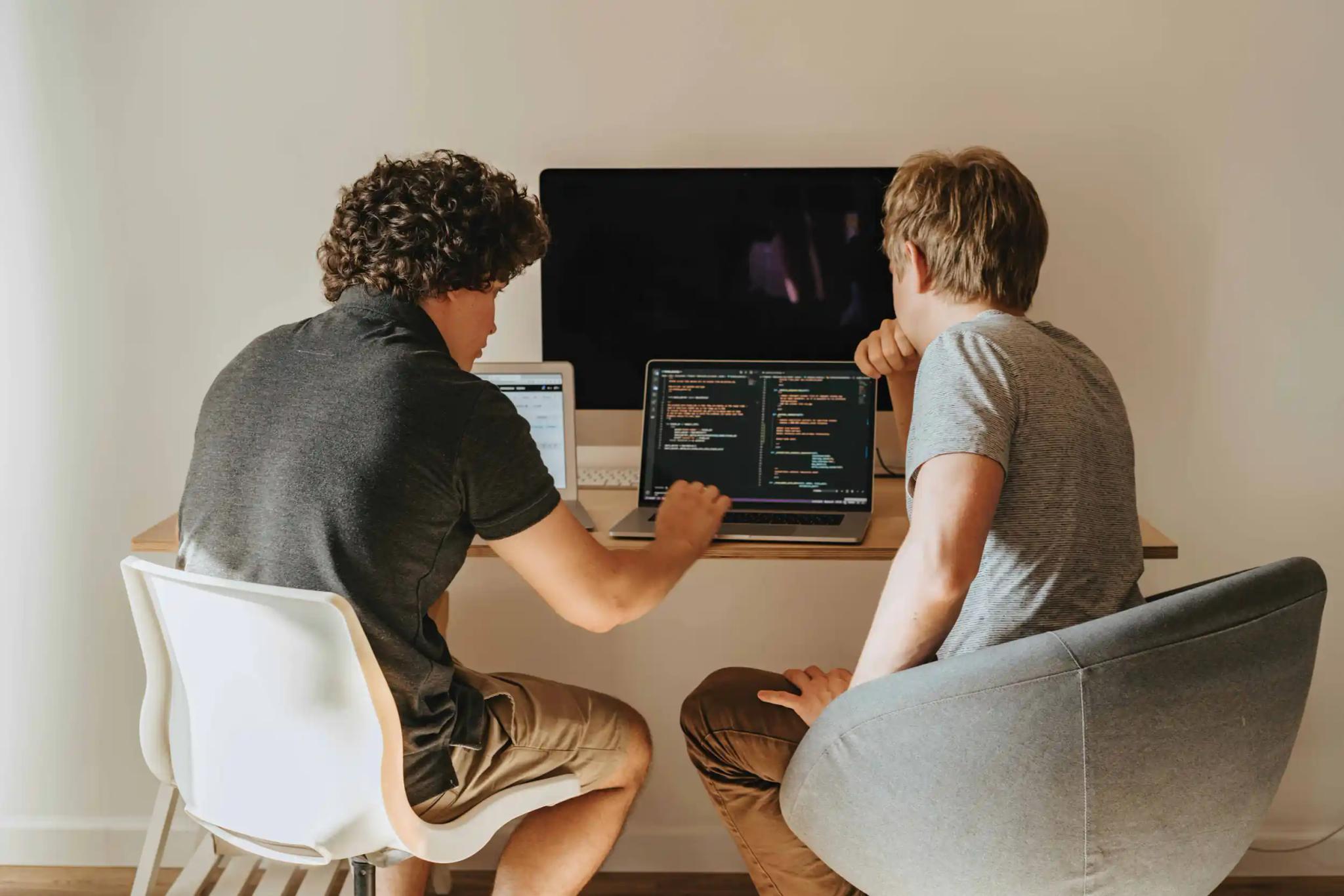 Two men sitting at a table working together on a laptop.