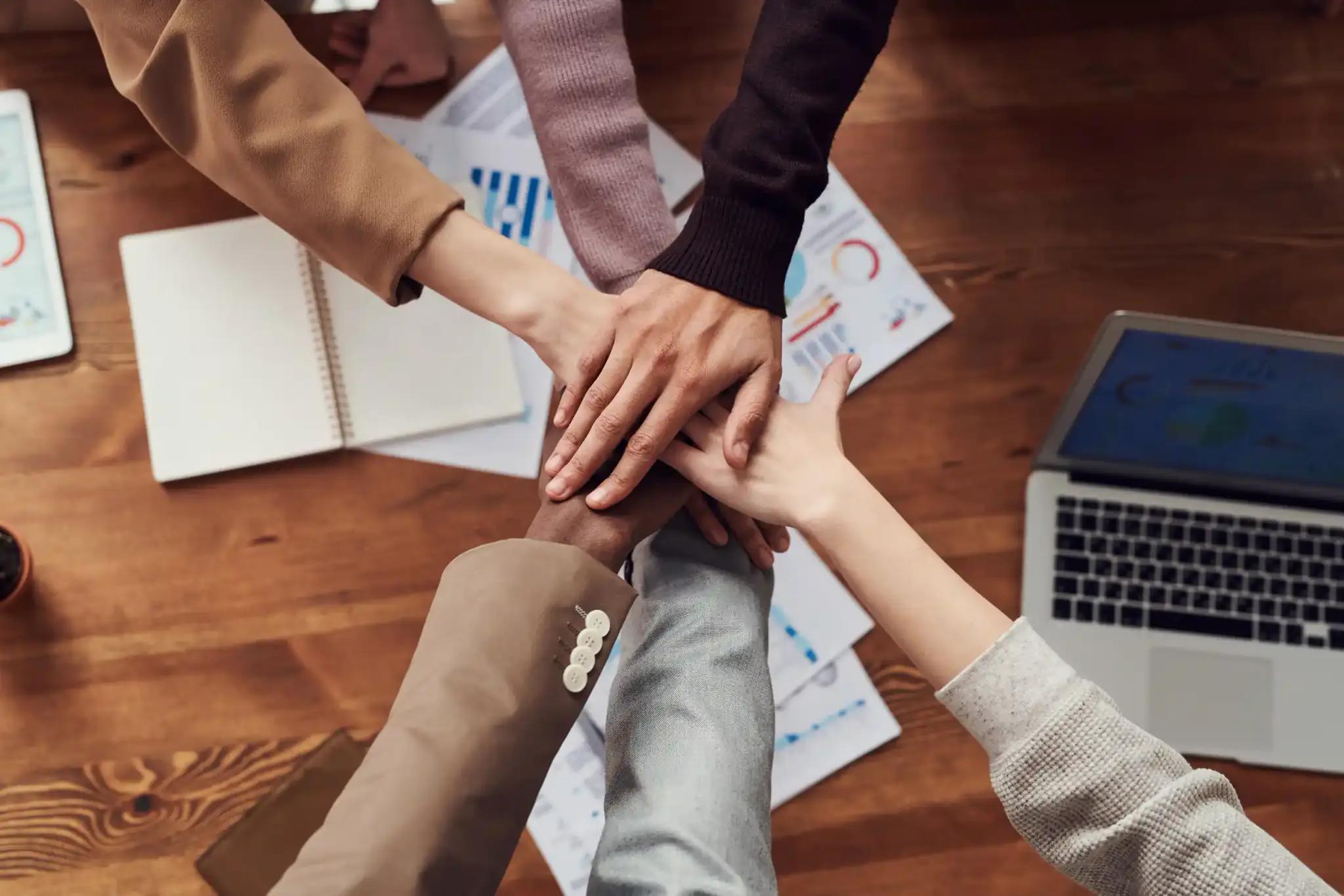 Multiple hands stacked together over a table symbolizing teamwork