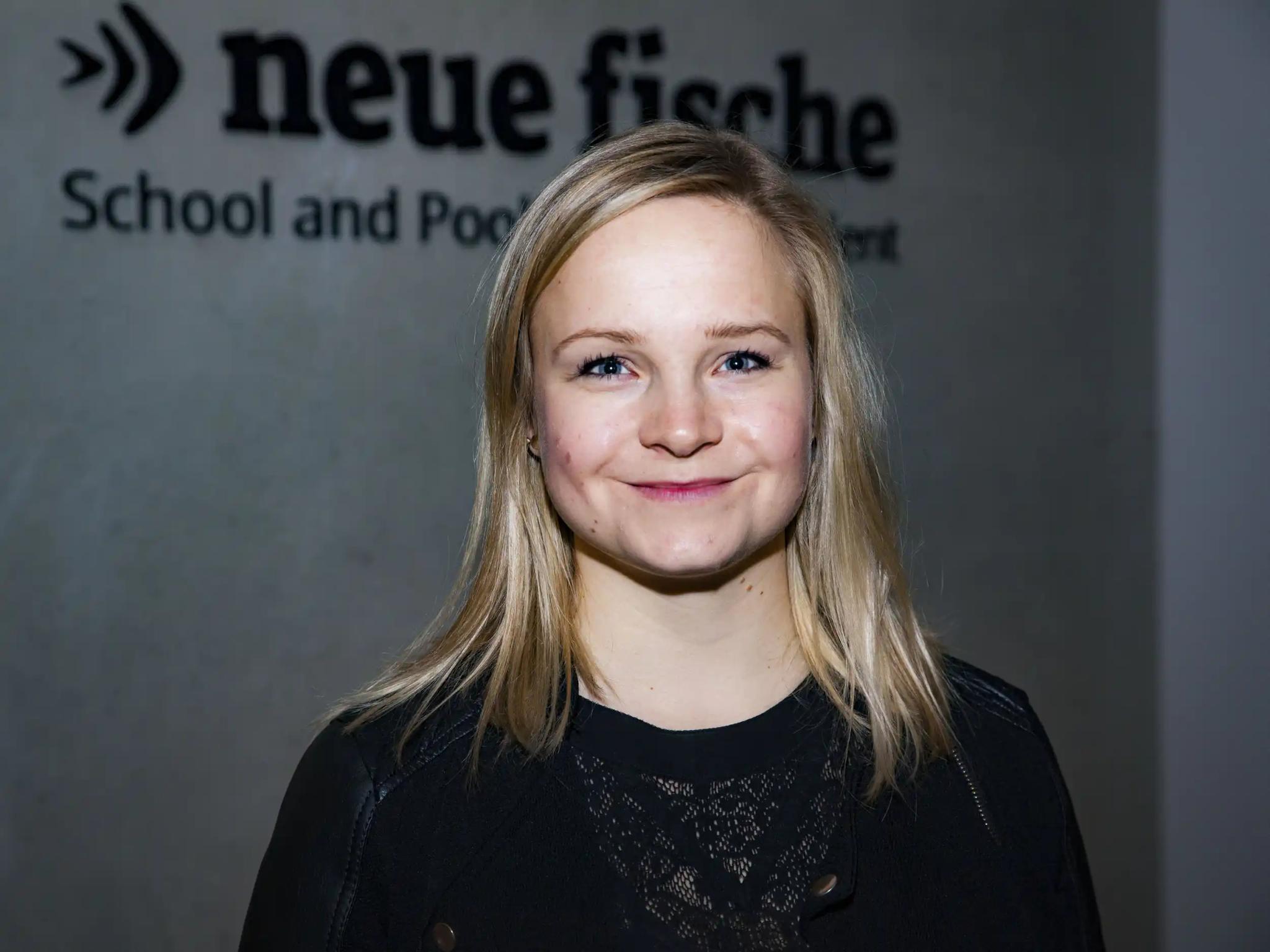 Portrait of a smiling woman in front of a wall with the 'neue fische' logo.