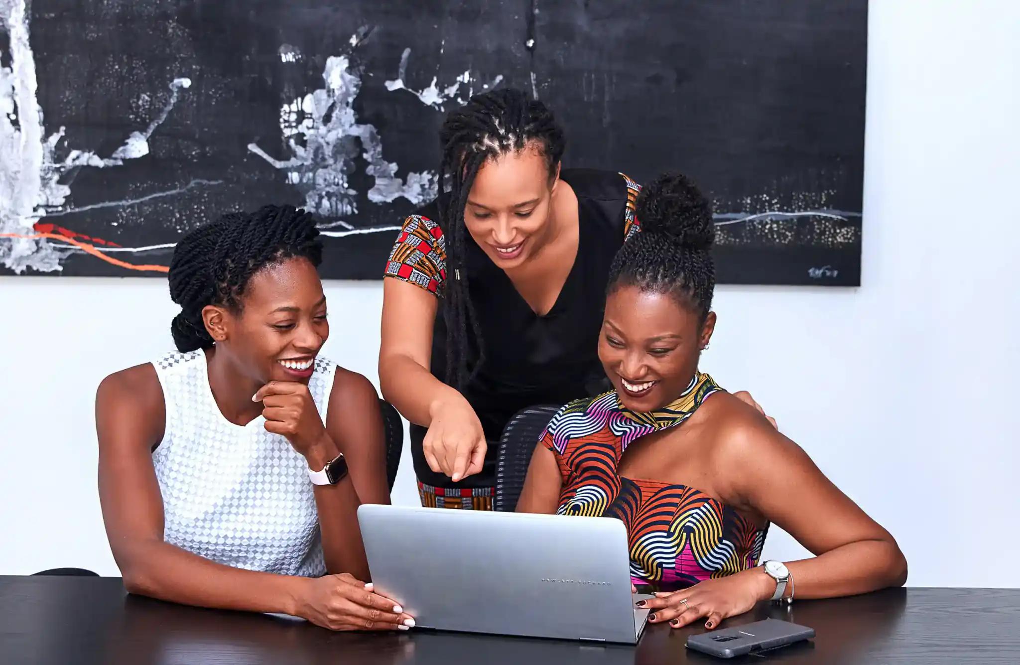 Three women looking at a laptop and smiling together.