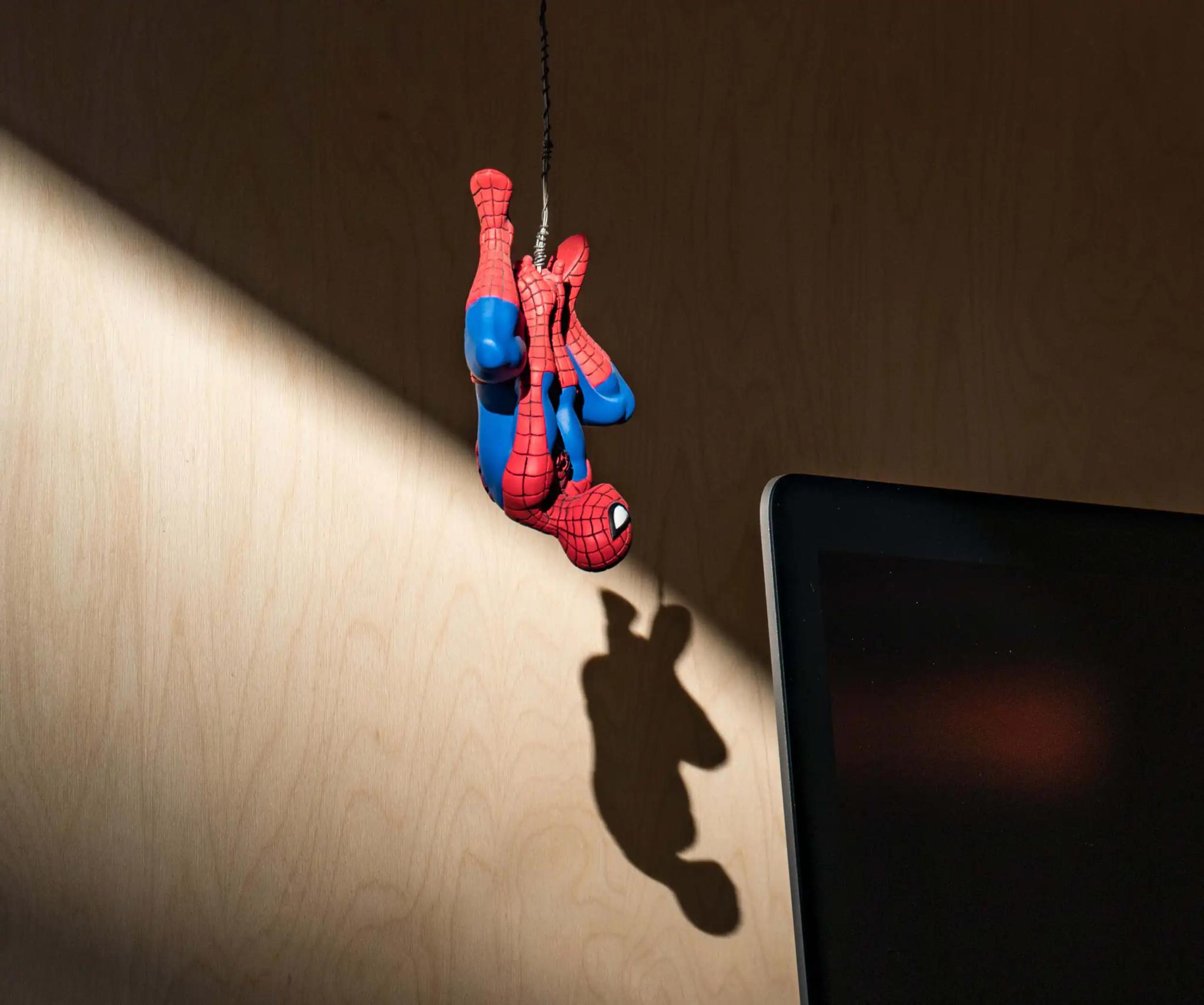 Spider-Man figure hanging upside down on a string next to a screen.