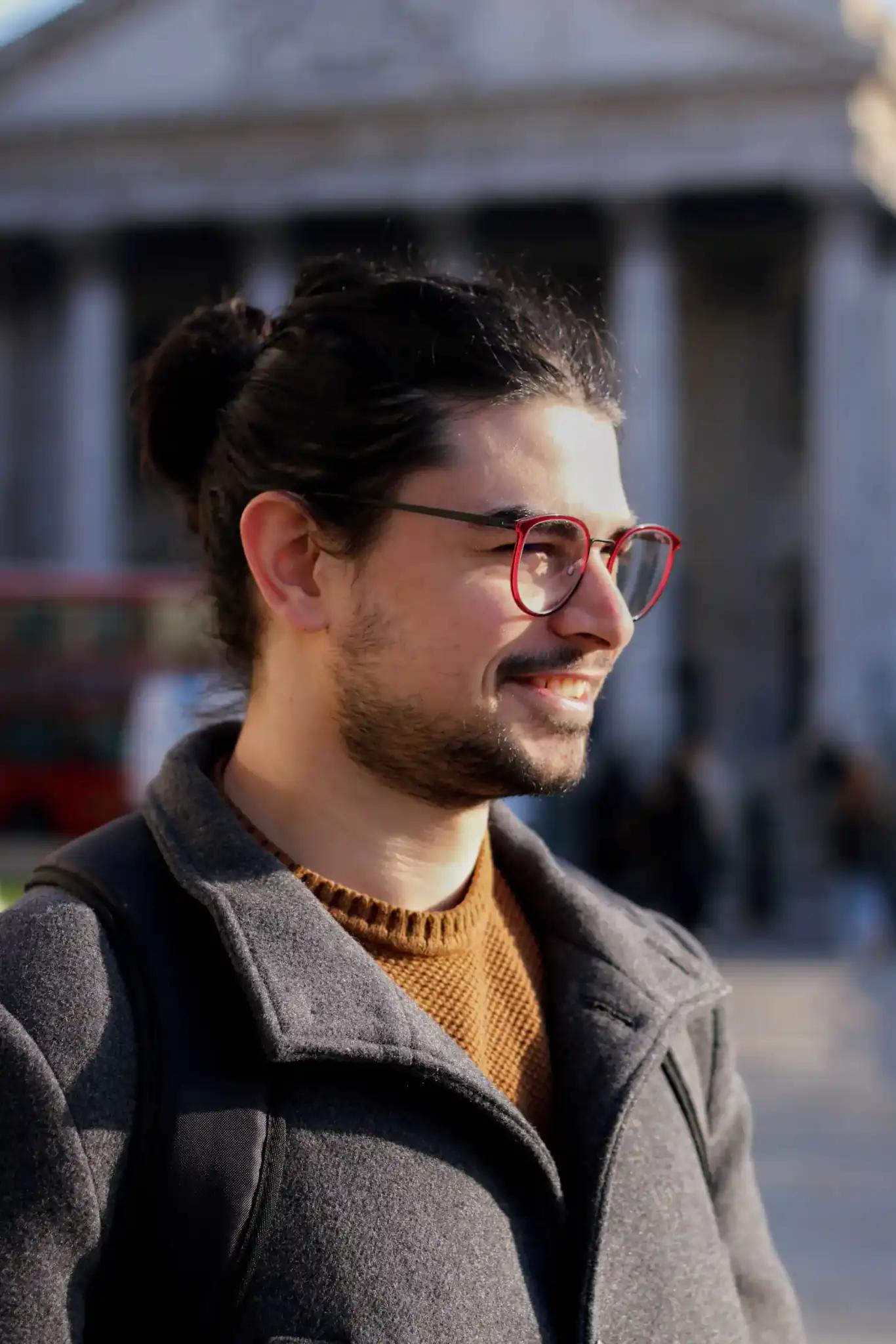 Portrait of a smiling man with red glasses and a bun outdoors