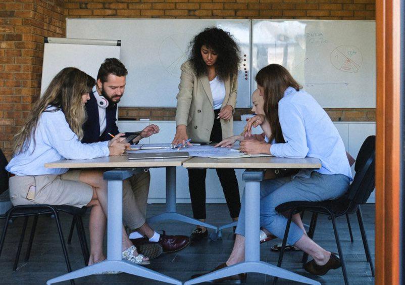 Gruppe von fünf Personen, die an einem Tisch in einem Meeting sind.