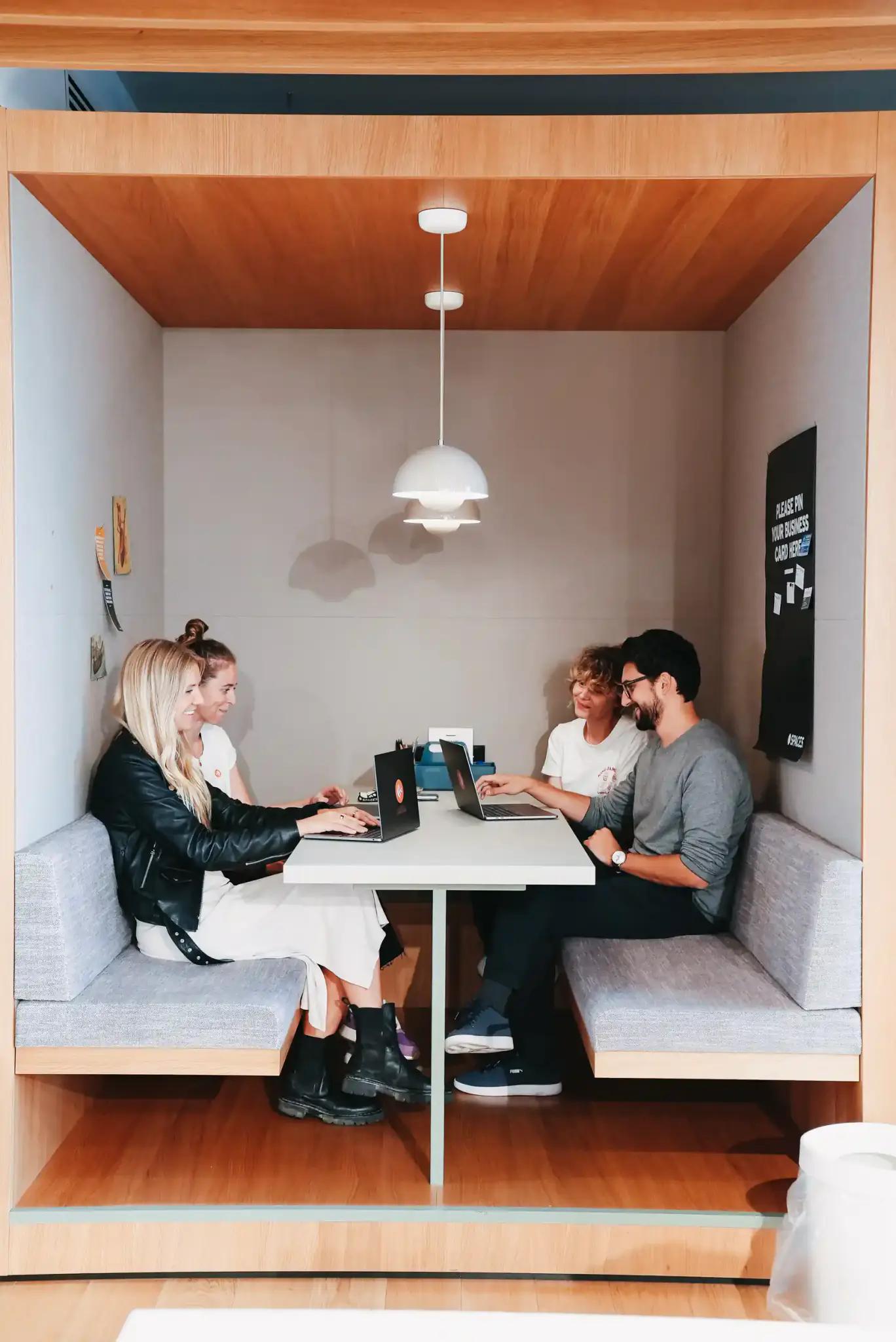 Vier Personen arbeiten an Laptops in einer modernen Sitznische.