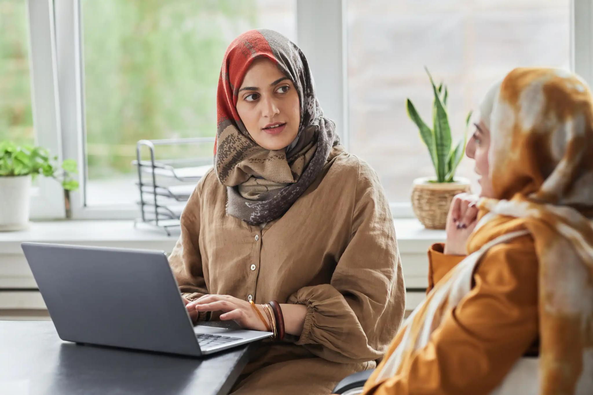 Zwei Frauen sprechen, eine benutzt einen Laptop.