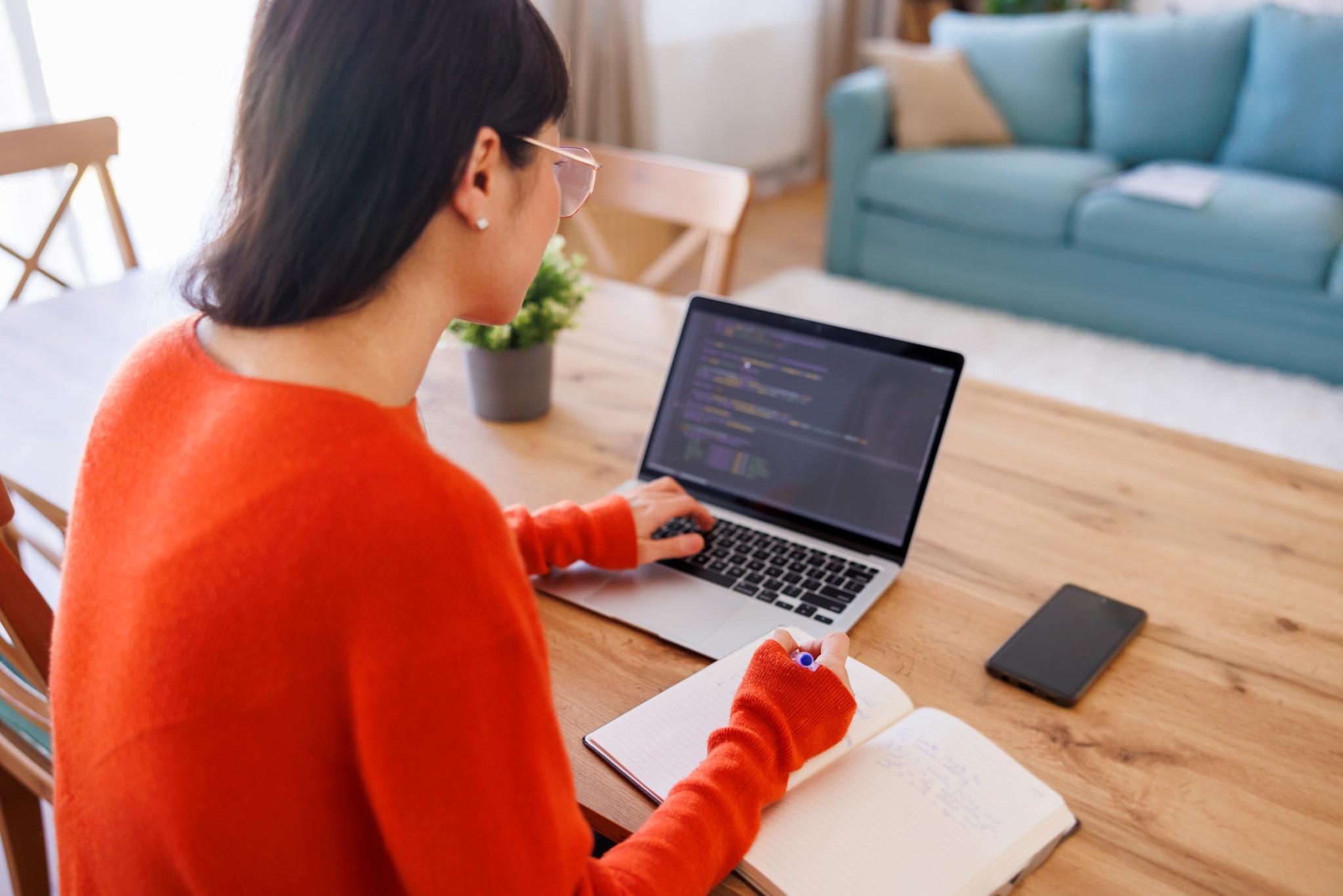 Frau programmiert an Laptop und macht Notizen.