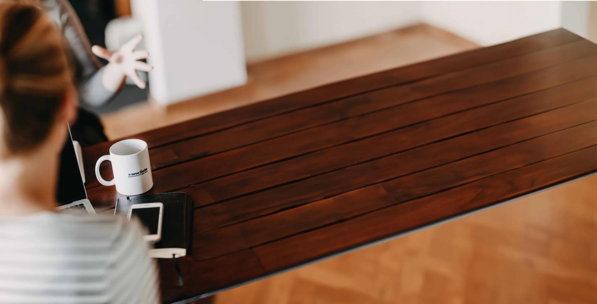 Person am Holztisch mit Tasse und Smartphone