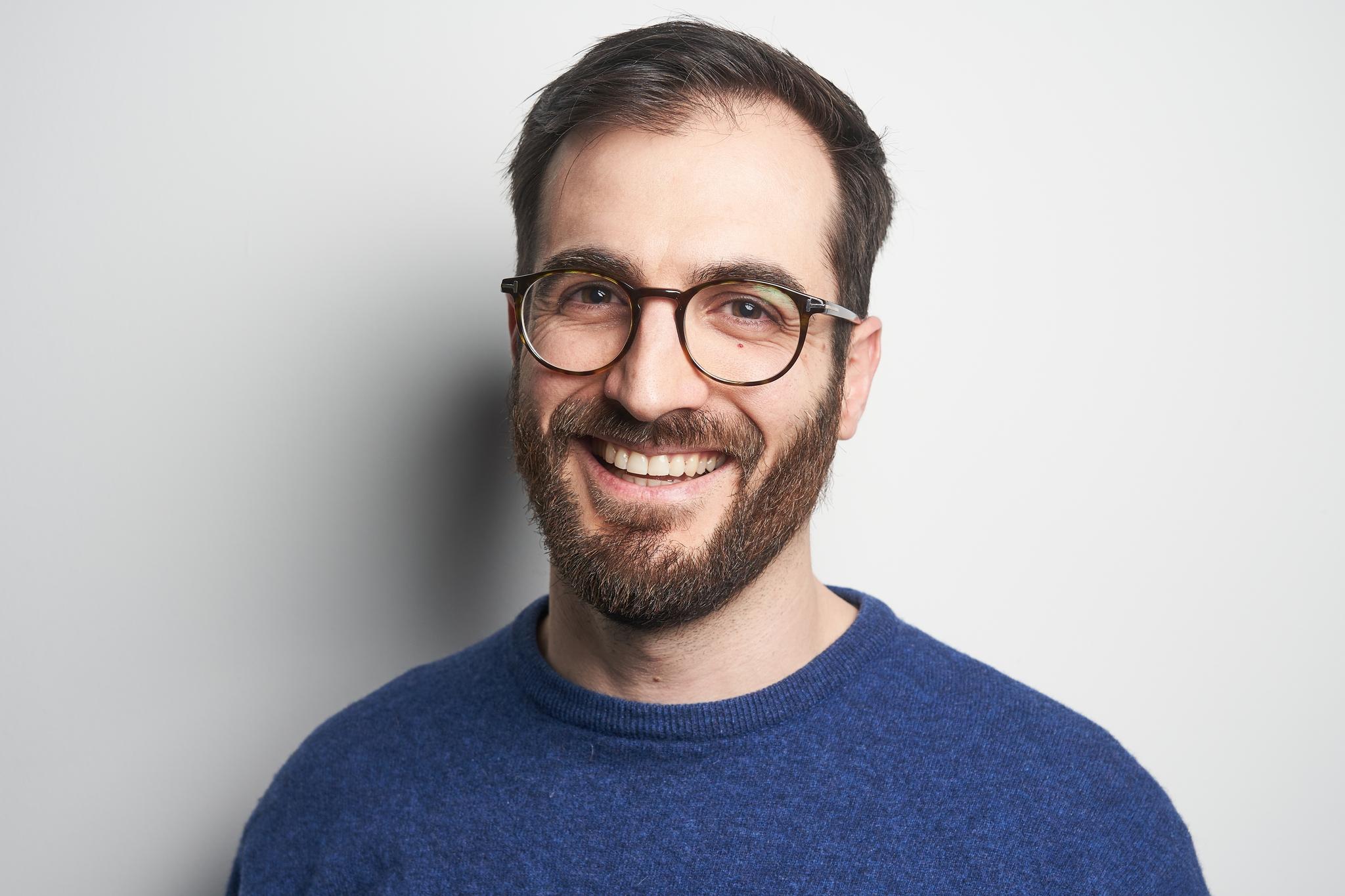 Man with glasses and blue sweater smiling