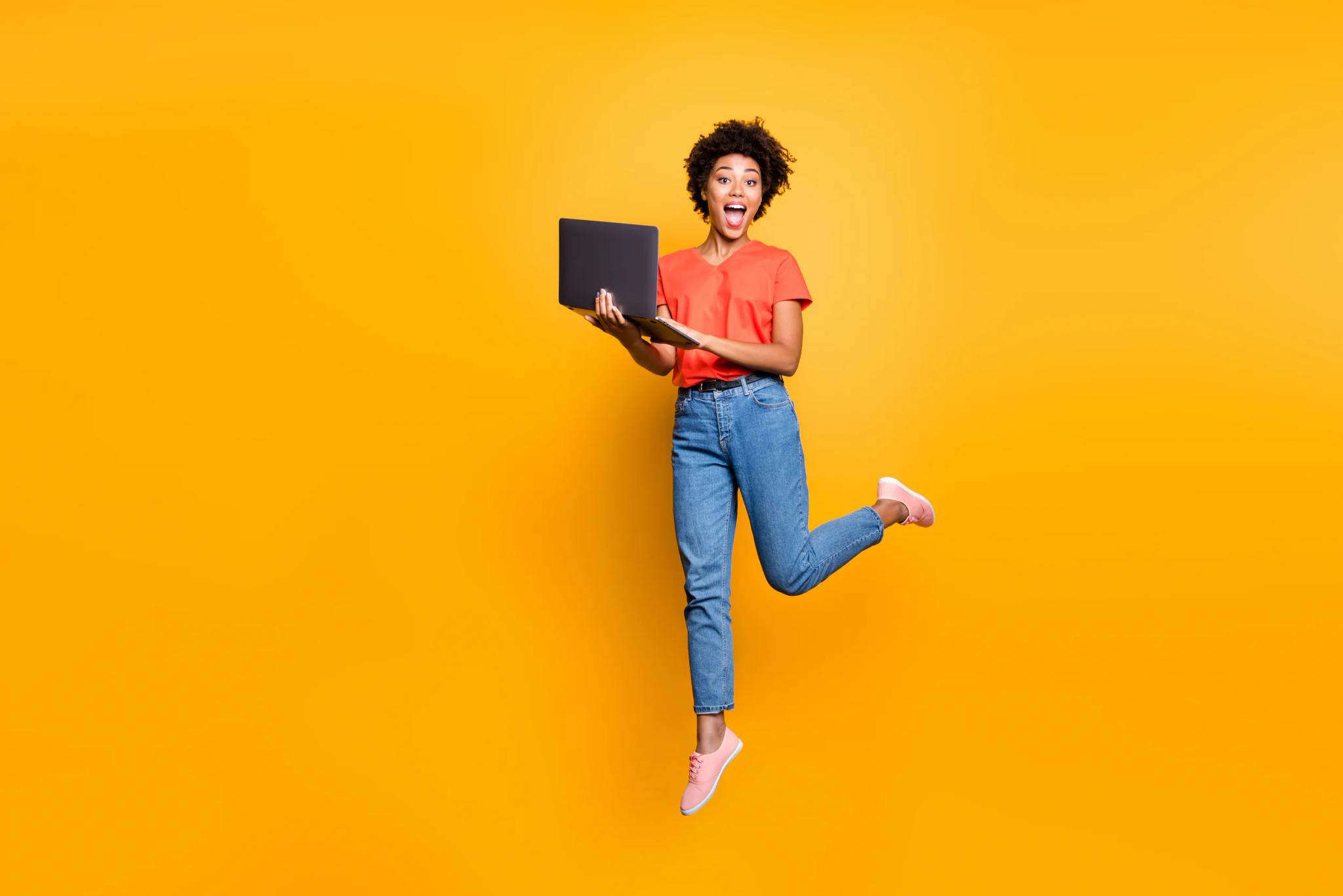 Frau springt mit Laptop vor gelbem Hintergrund