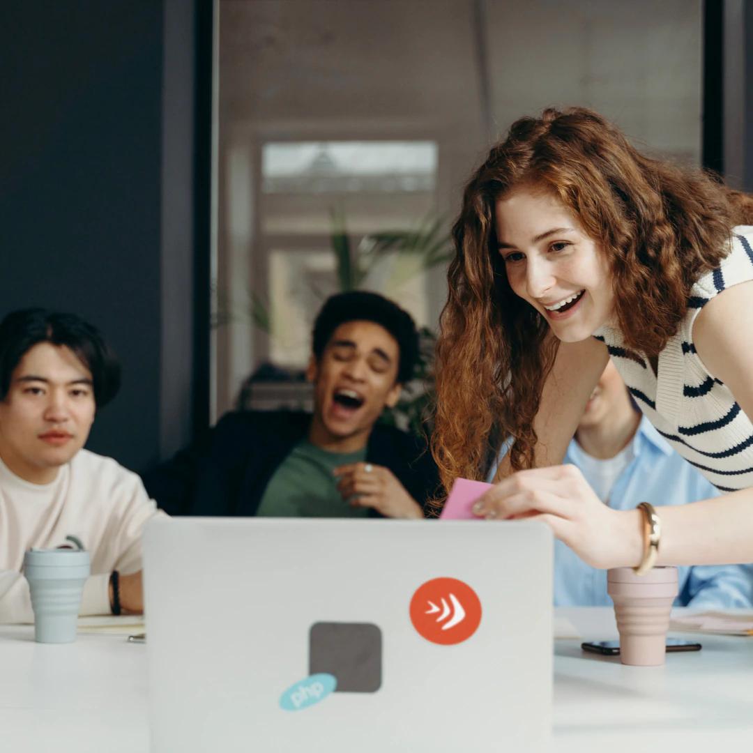 Group of young people laughing and having fun around a laptop.
