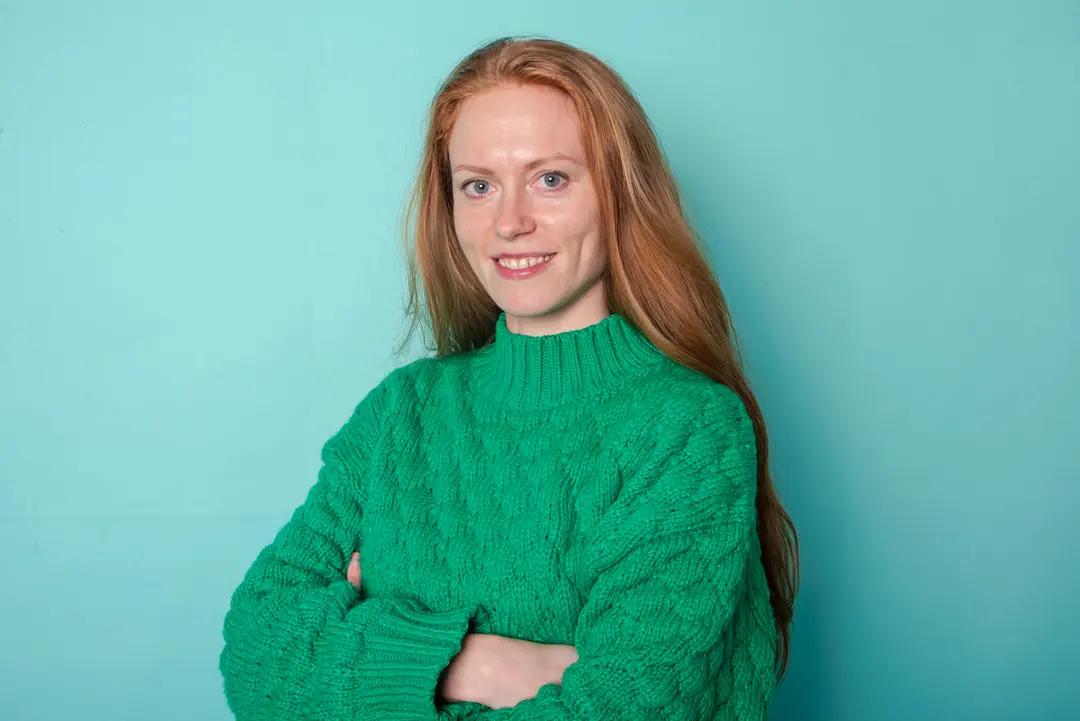 Woman in green sweater against blue background.
