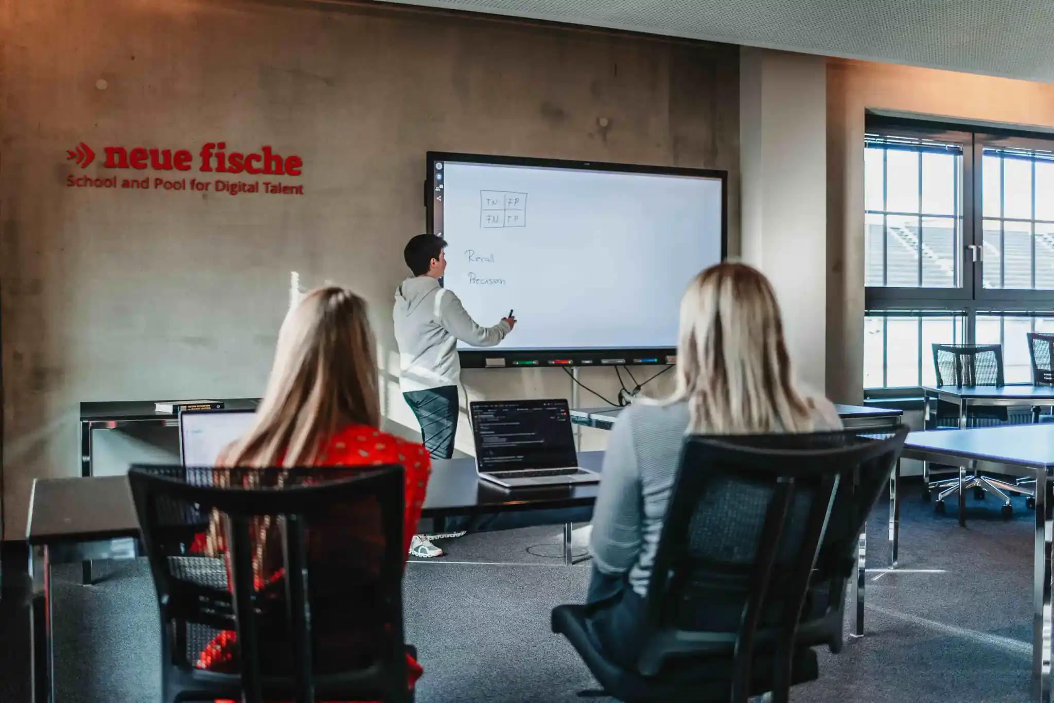 Man explaining something on a digital whiteboard to two people in an office.