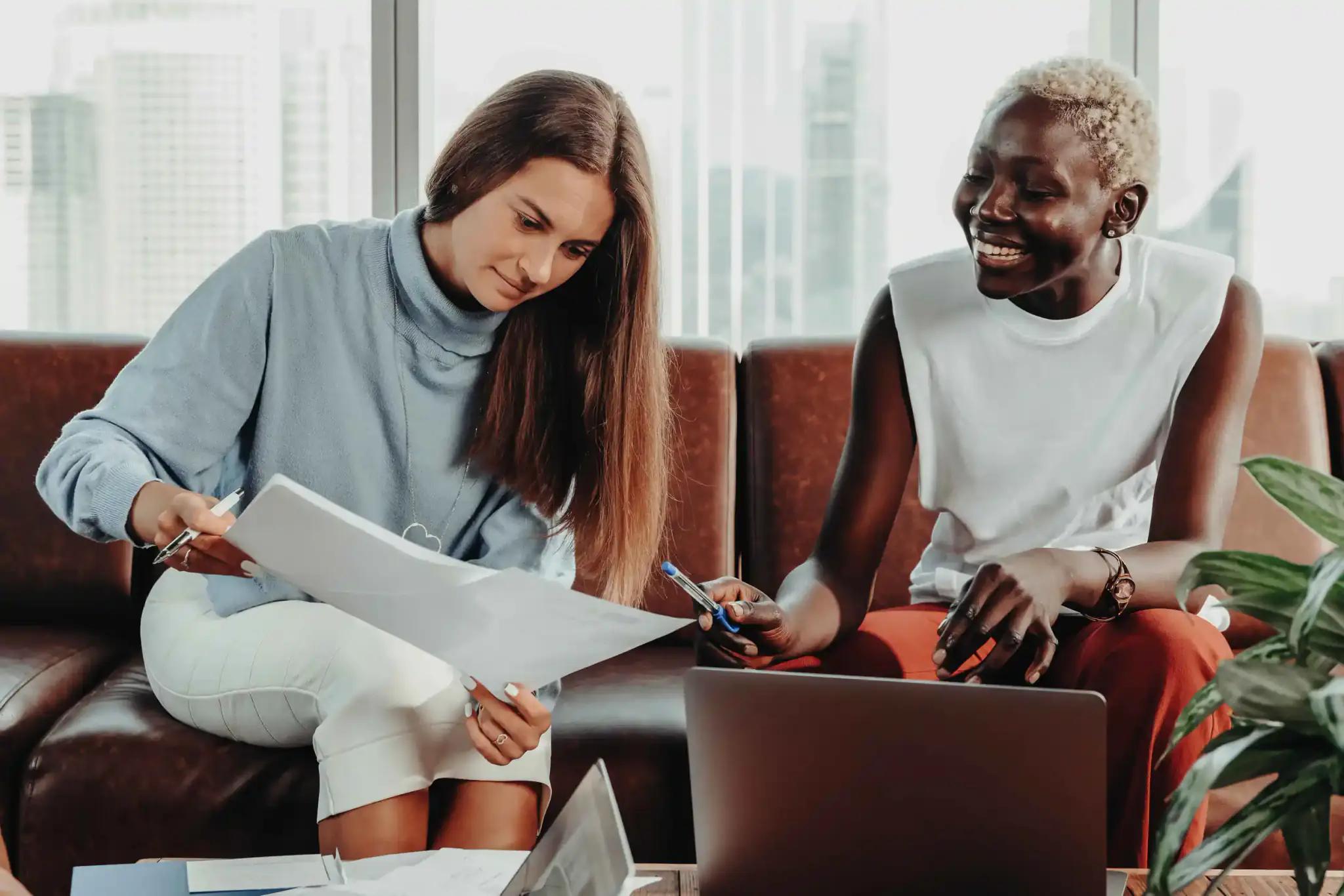 Two women working together with laptop and documents.
