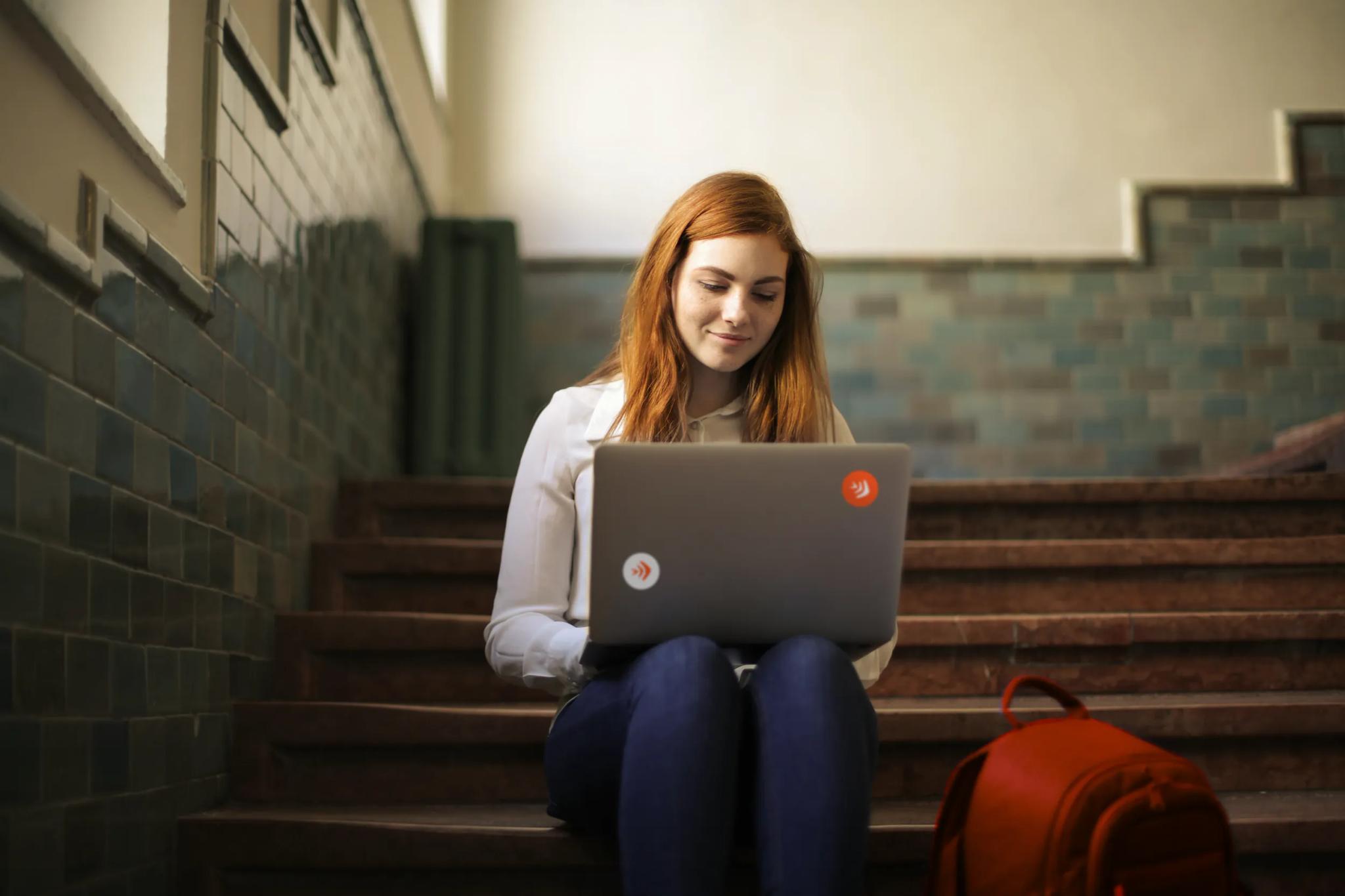Junge Frau sitzt auf Treppe und arbeitet am Laptop.