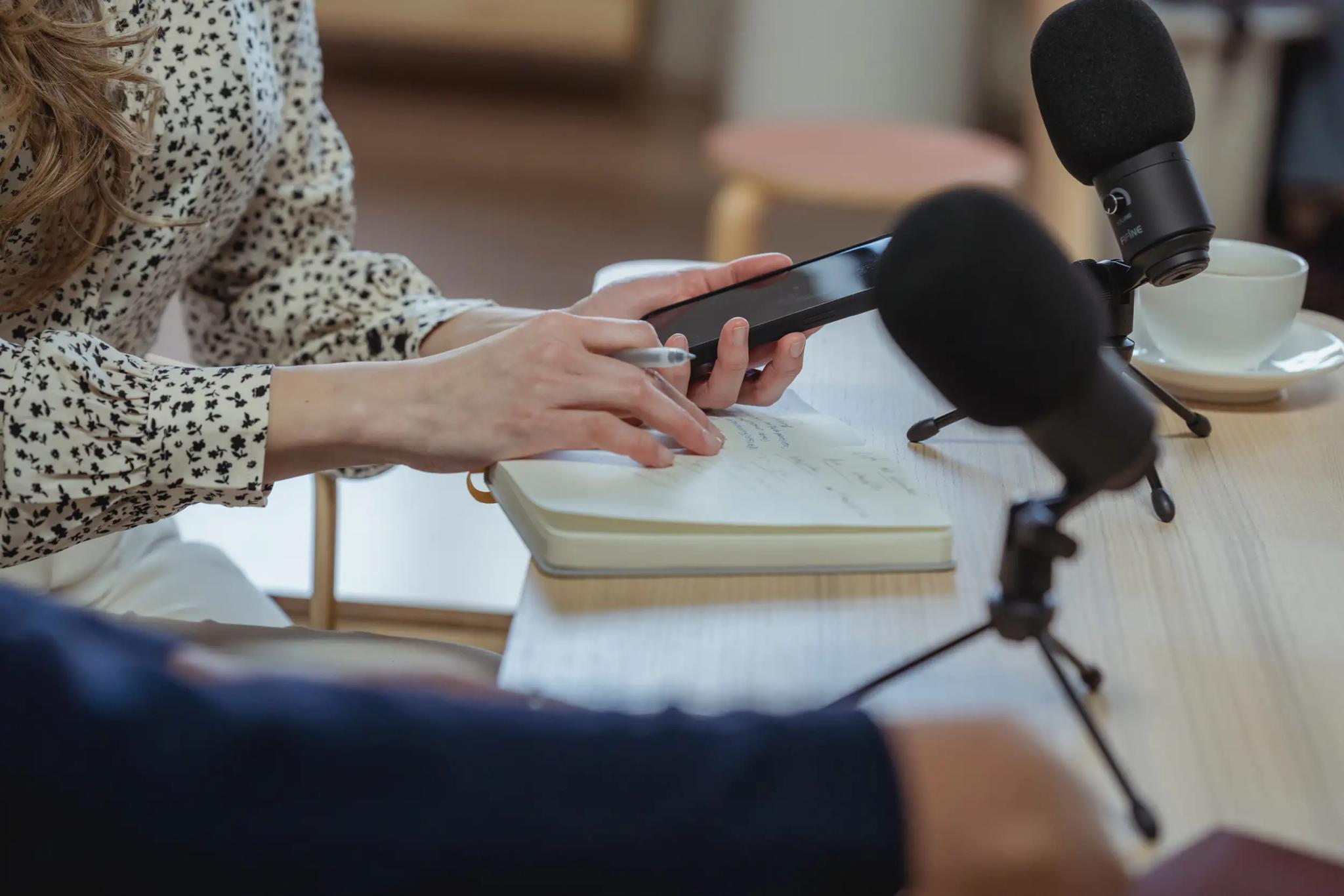 Person setting up smartphone for podcast recording next to microphones on table.