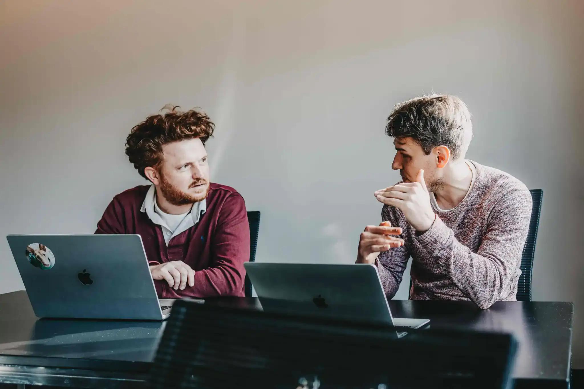 Two men discussing work with laptops.