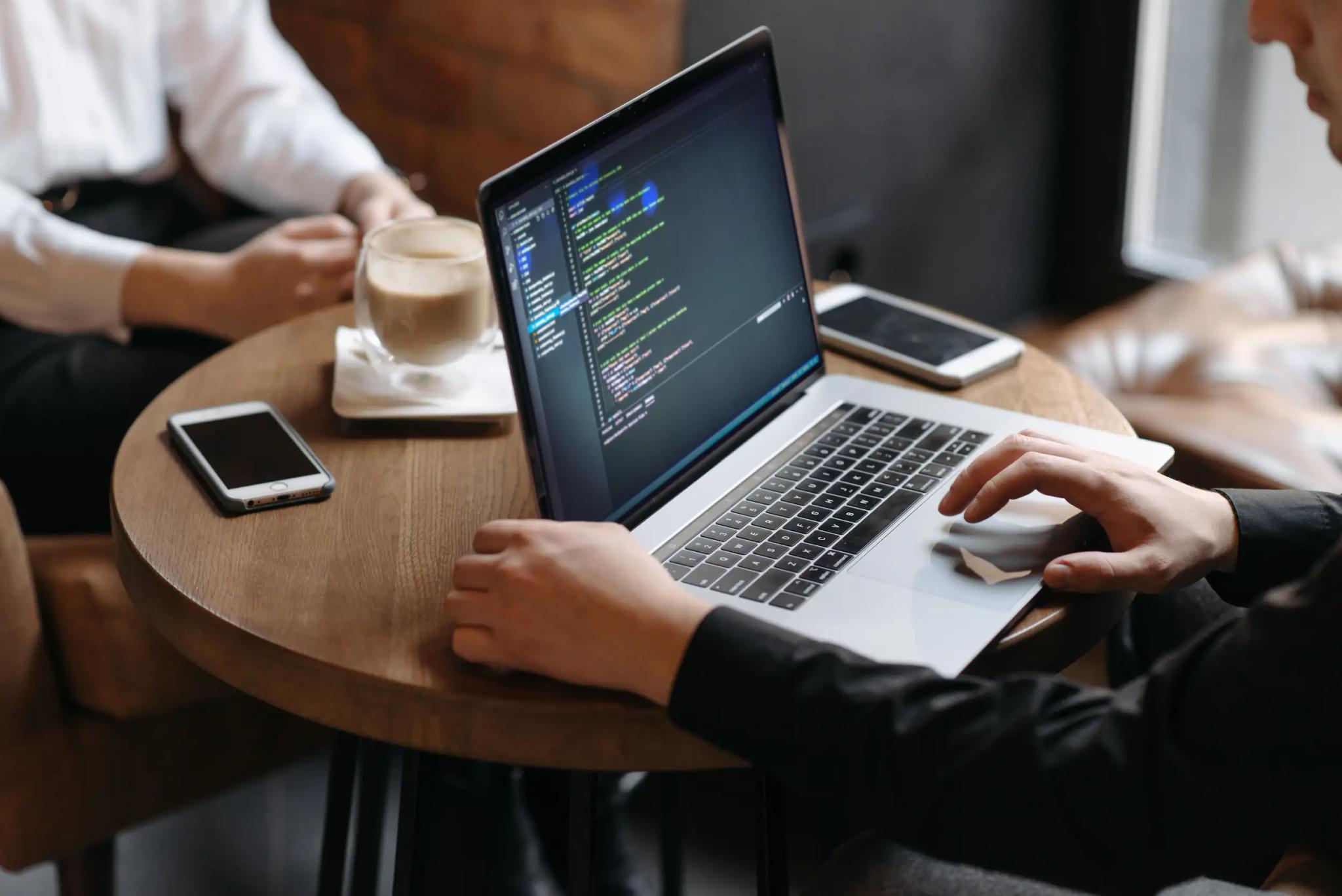 Person arbeitet an Laptop mit Programmiercode in Café