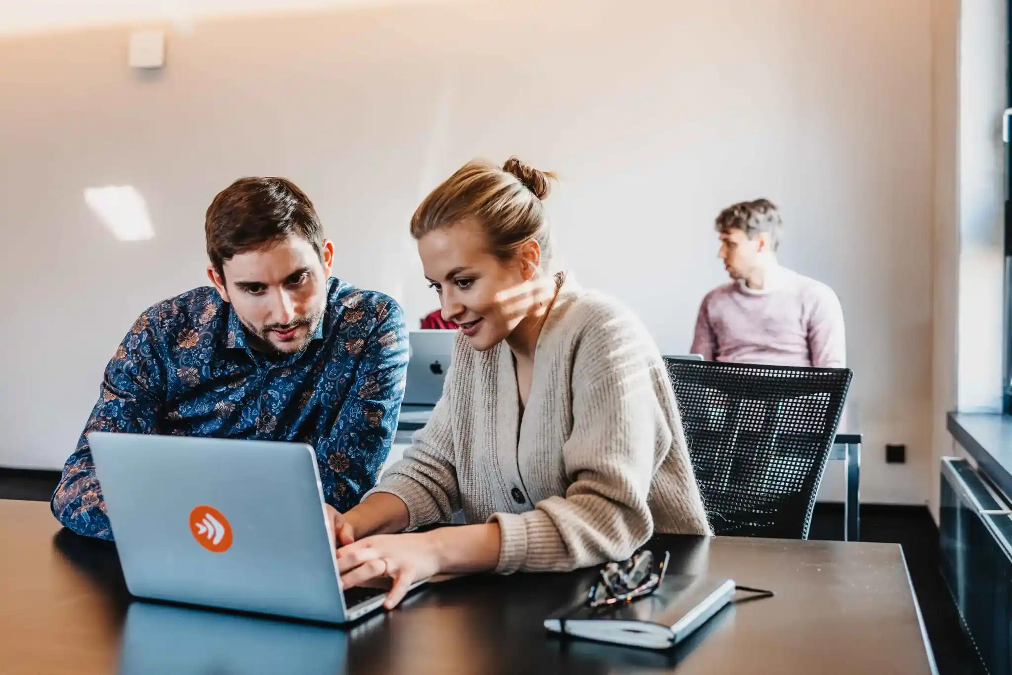 Two people working together on a laptop in an office.
