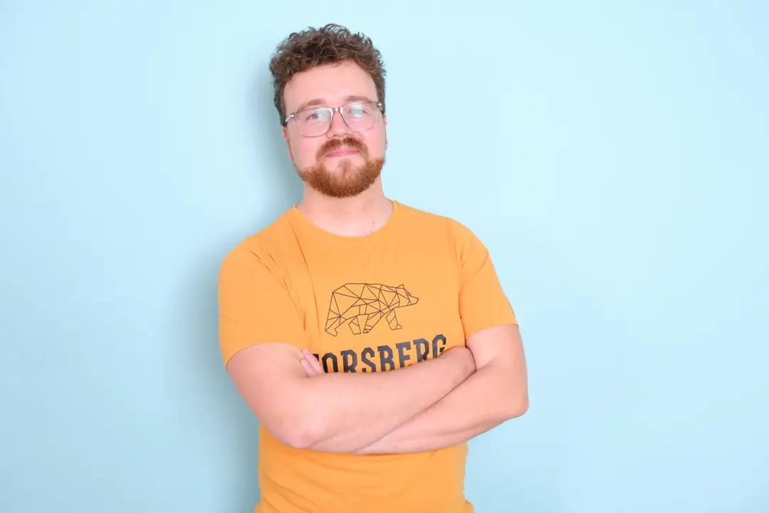 Man with glasses wearing an orange t-shirt against a blue background