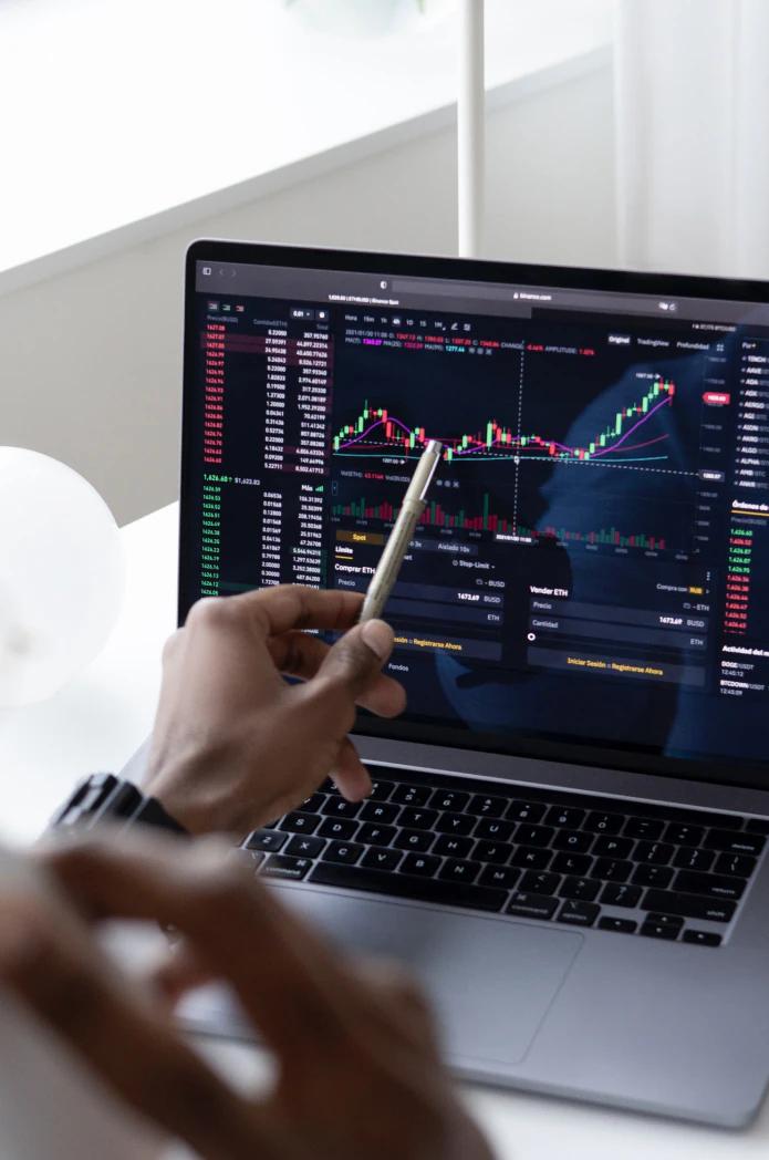 Laptop mit Finanzdiagrammen und Hand mit Stift