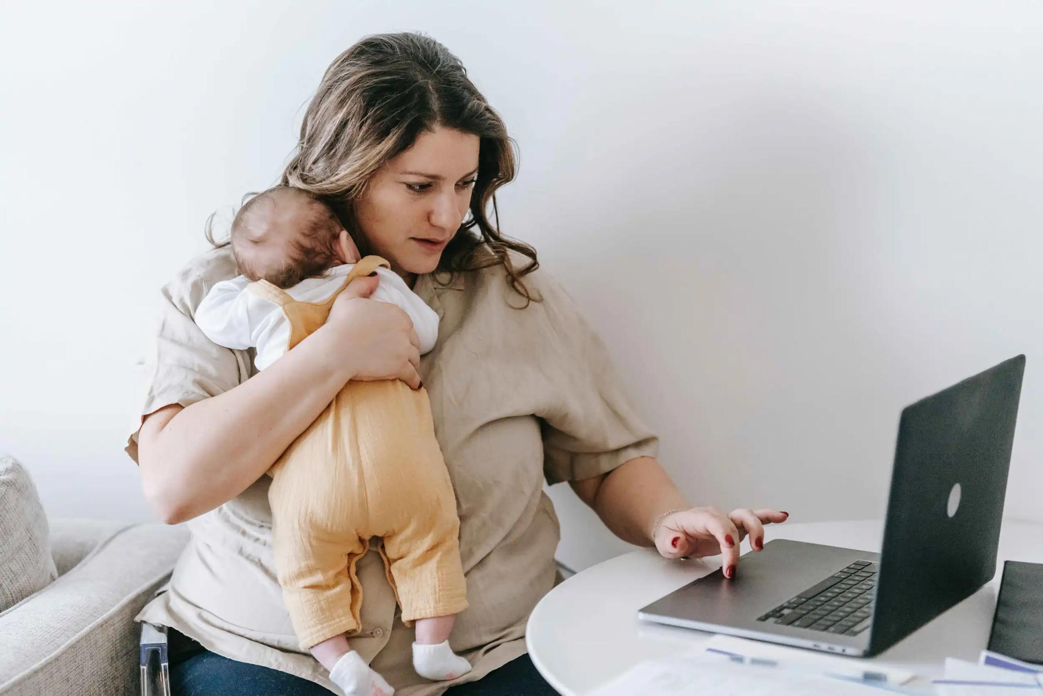Woman holding baby and working on laptop