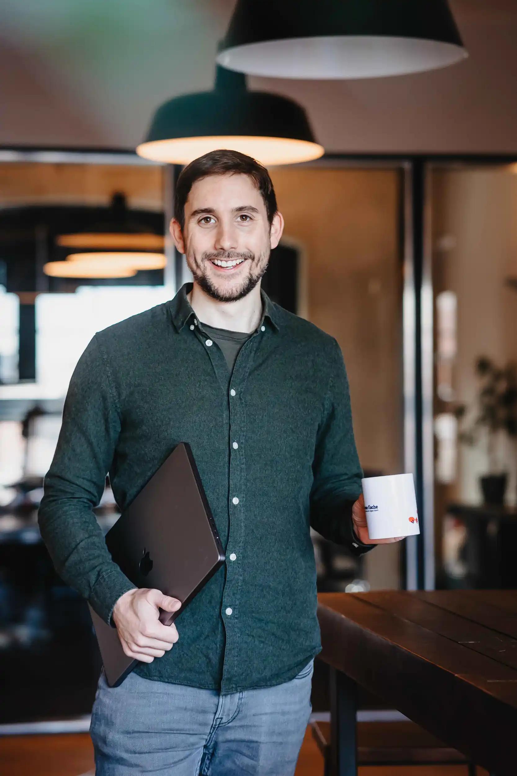 Lächelnder Mann hält Laptop und Tasse in Büro
