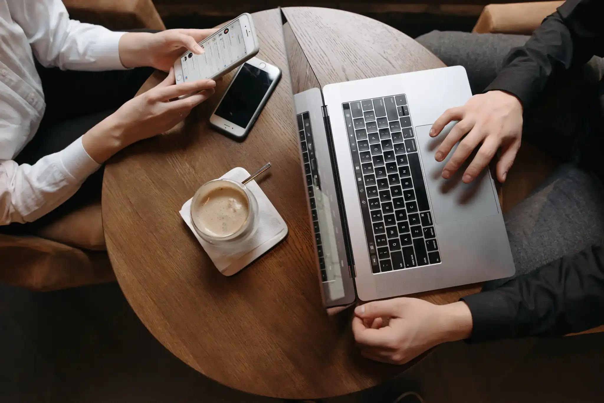 Two people at a round table with laptop, phone, and coffee.