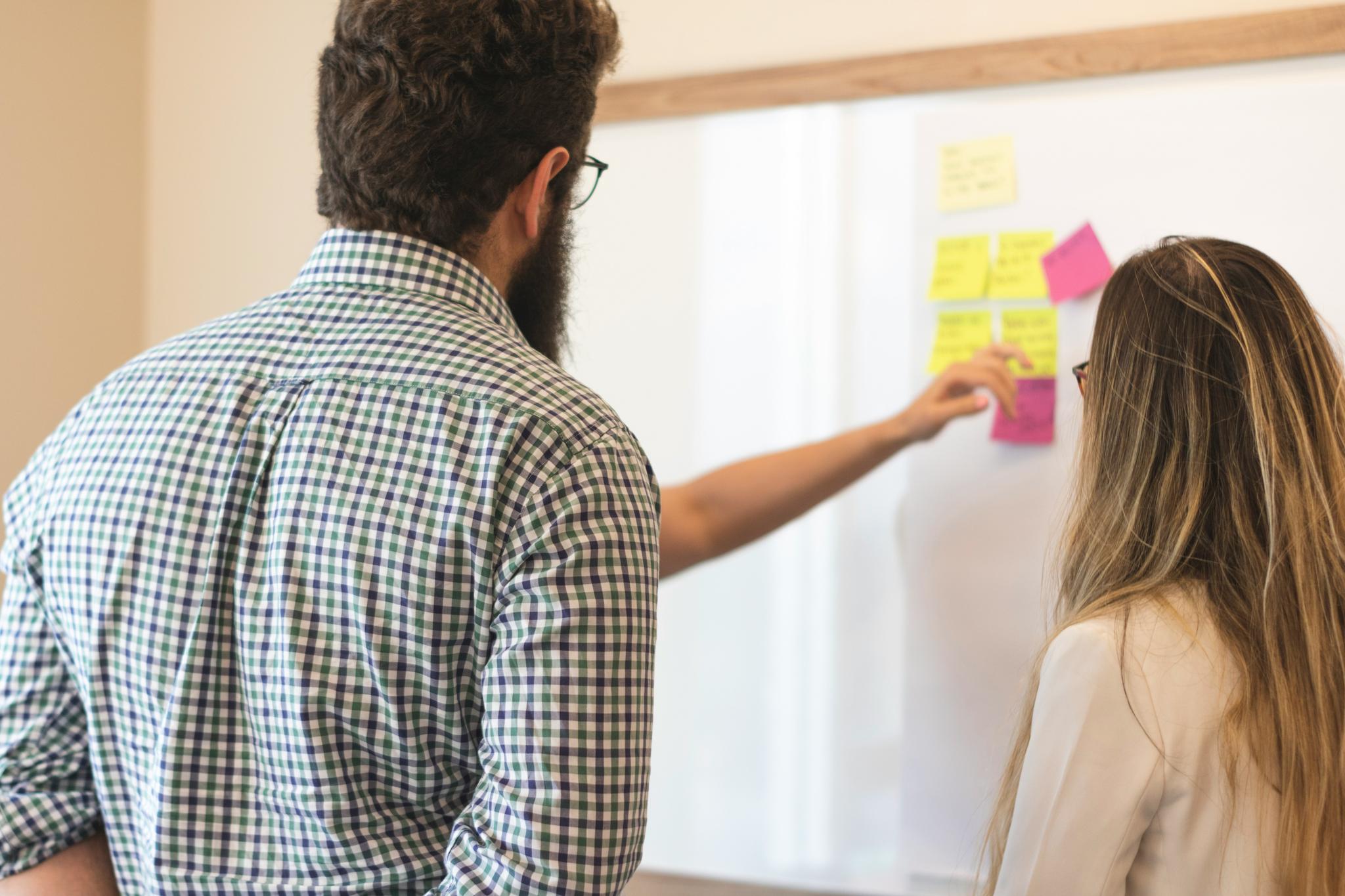 Two people looking at and organizing sticky notes on a wall.