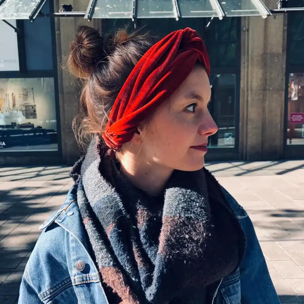 Portrait of a woman wearing a red headband and scarf outdoors.