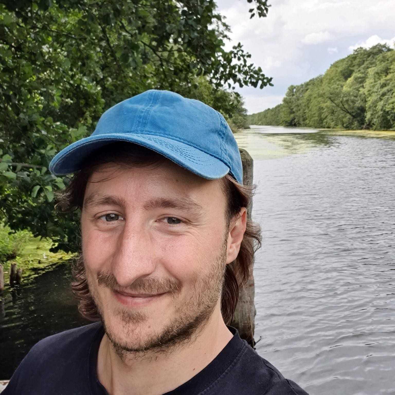 Mann mit blauer Mütze am Flussufer