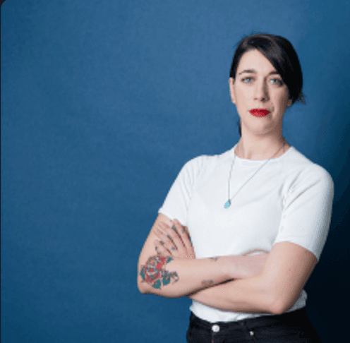 Woman in white t-shirt with tattooed arm against blue background.