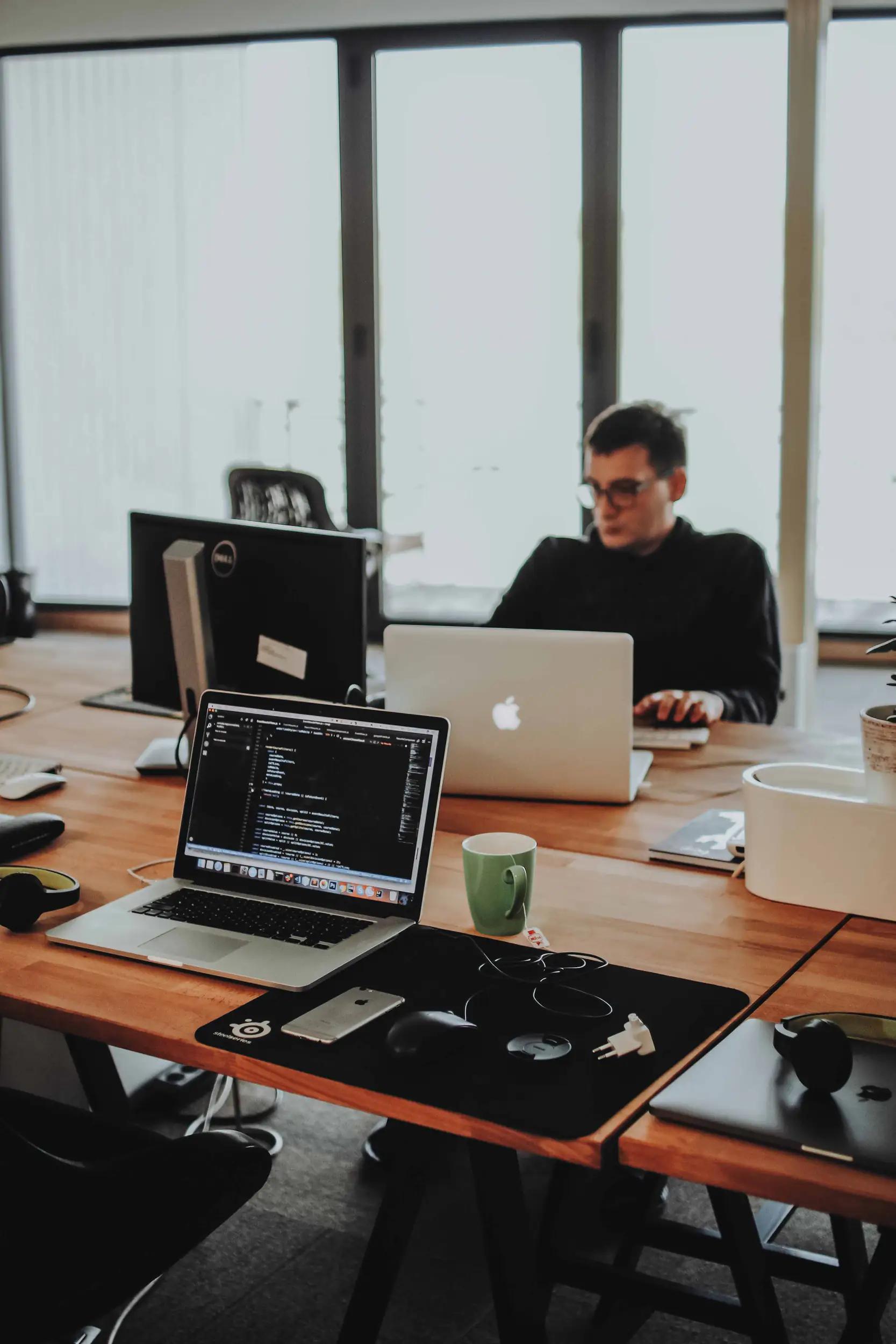 Person working on laptop in office with computers on the desk.