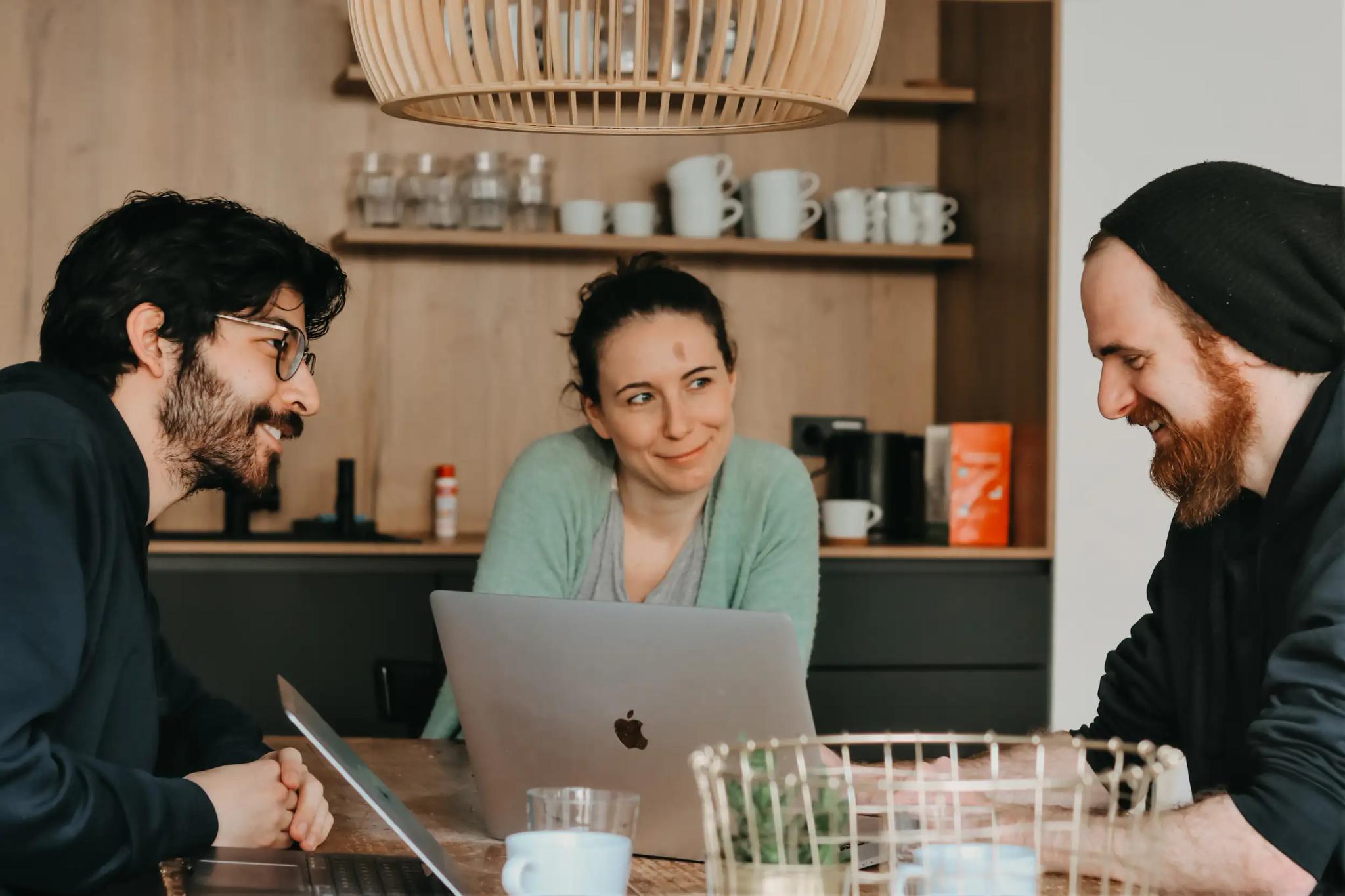 Three people talking together in a meeting with laptops