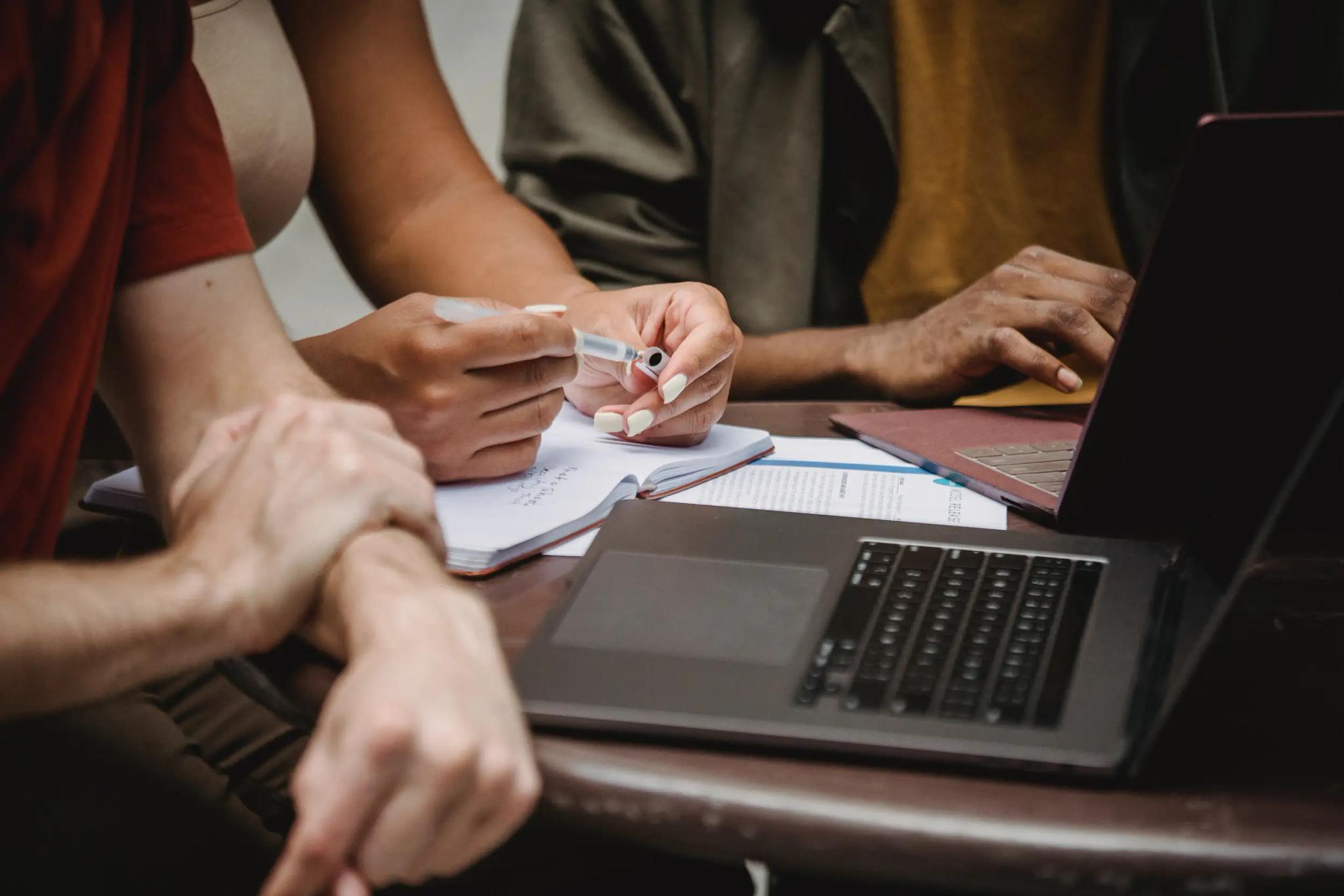 People working together on a laptop and taking notes.