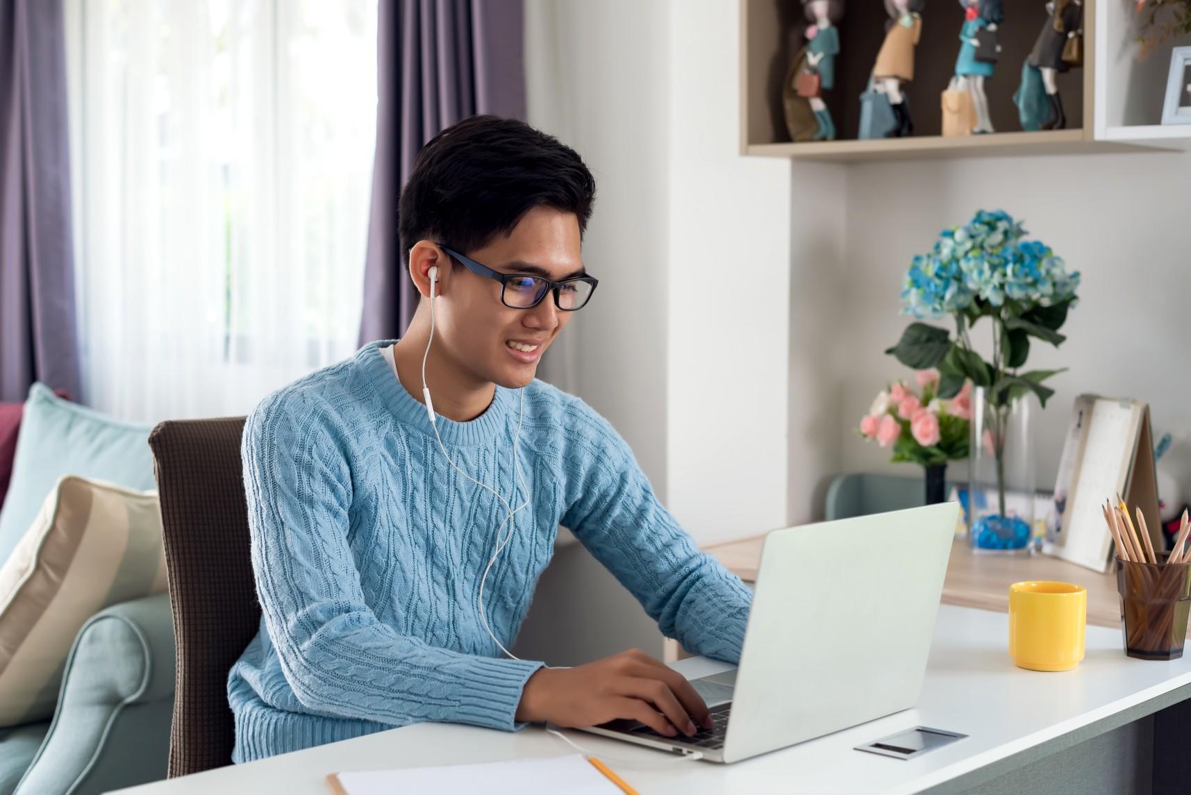 Junger Mann mit Brille arbeitet mit Kopfhörern am Laptop.