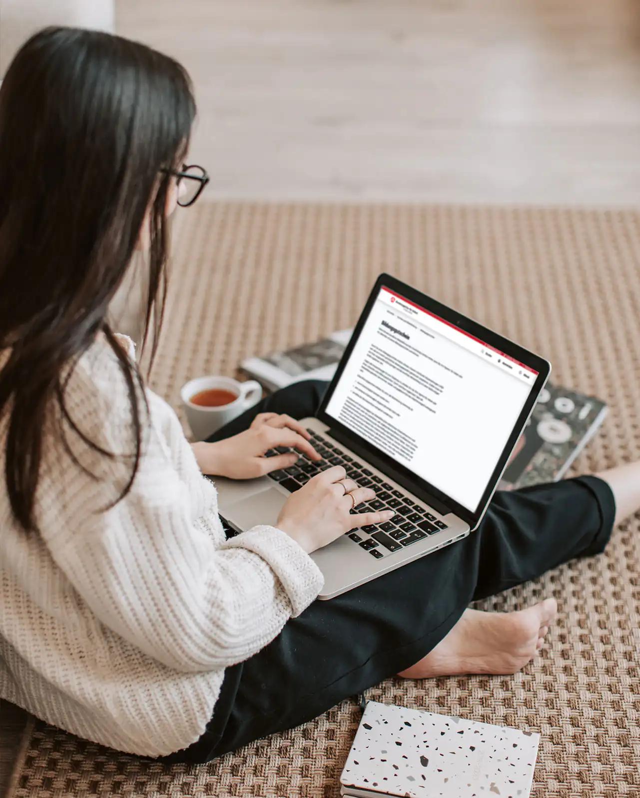 Frau arbeitet auf Laptop zu Hause sitzend.