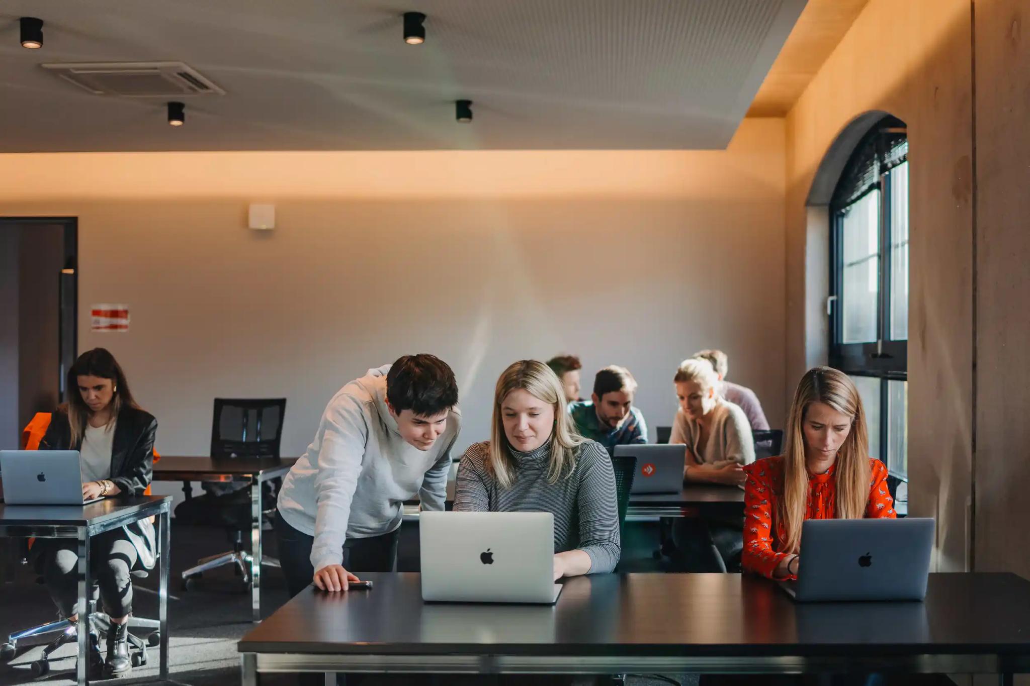 Menschen arbeiten zusammen an Laptops in einem Klassenraum.