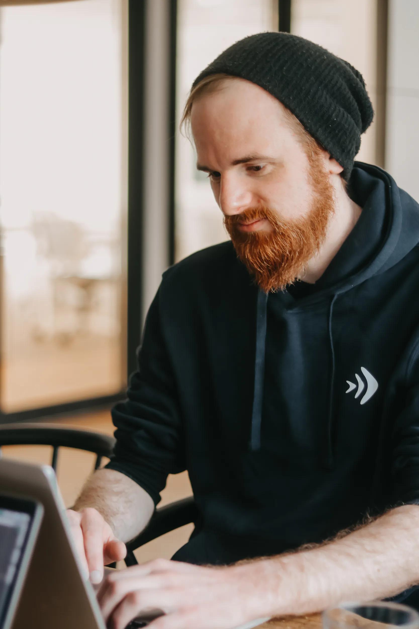 Man with black beanie working on laptop.