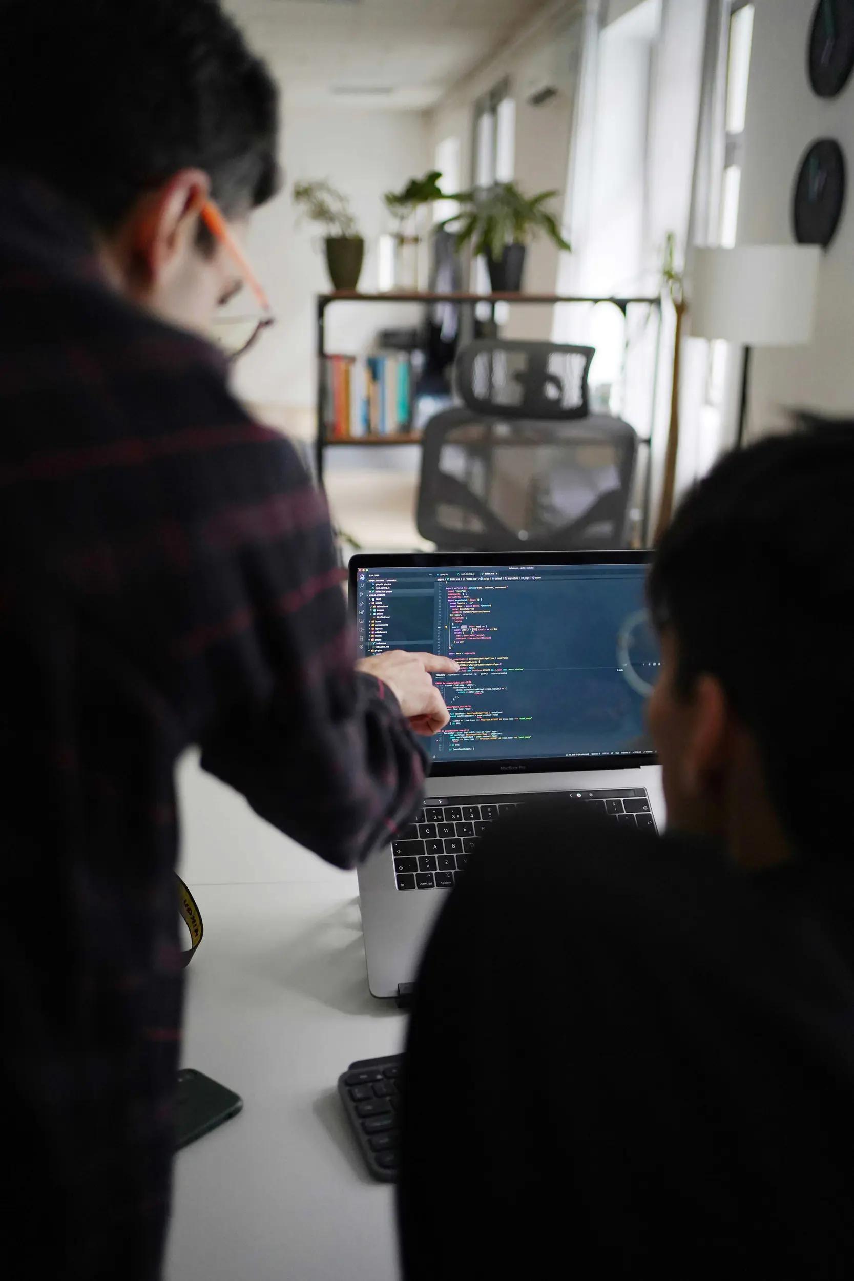 Two people working together on a laptop with programming code on the screen.