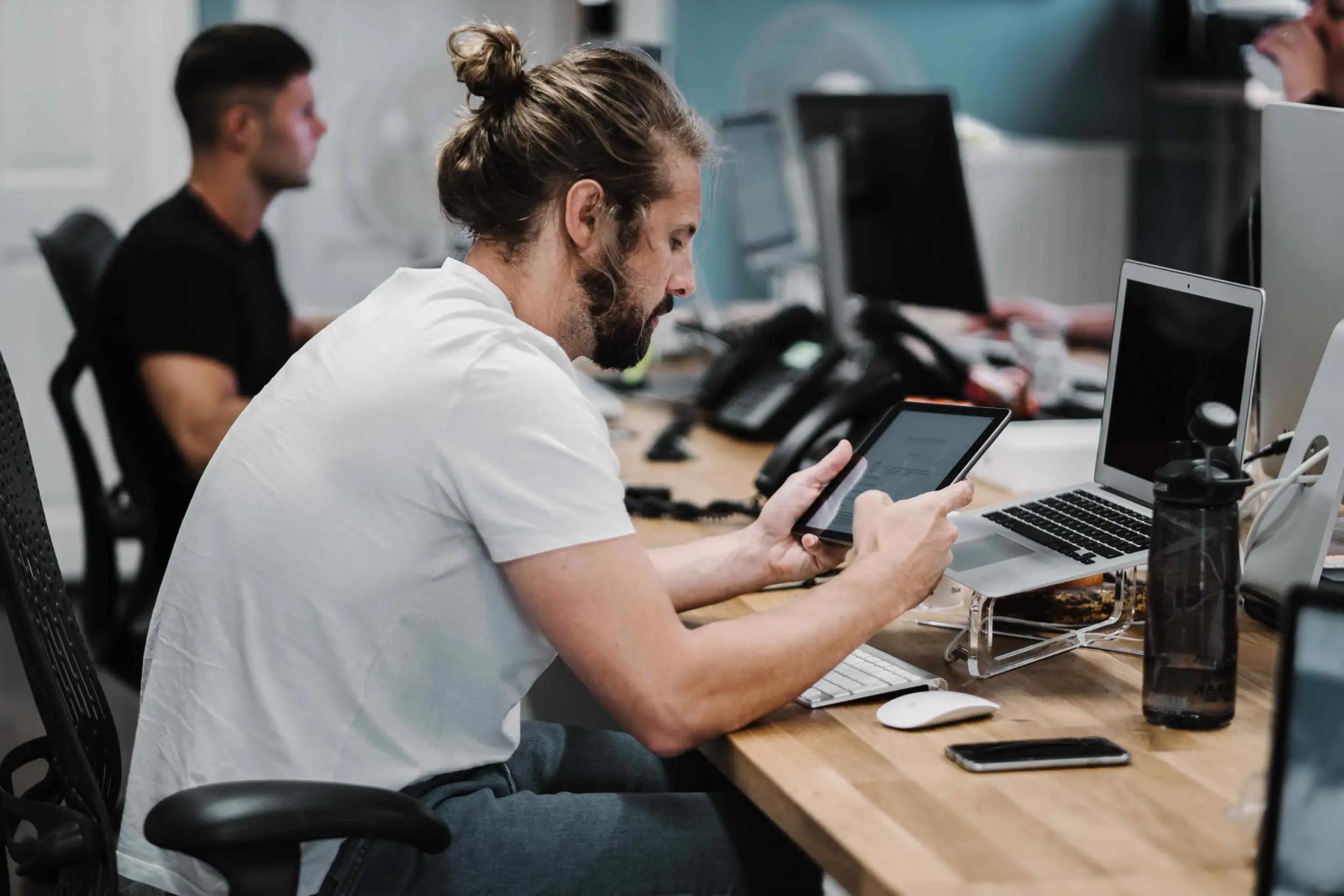Mann im Büro arbeitet mit Tablet und Laptop.
