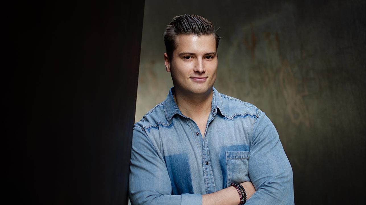 Young man in denim shirt against dark background.