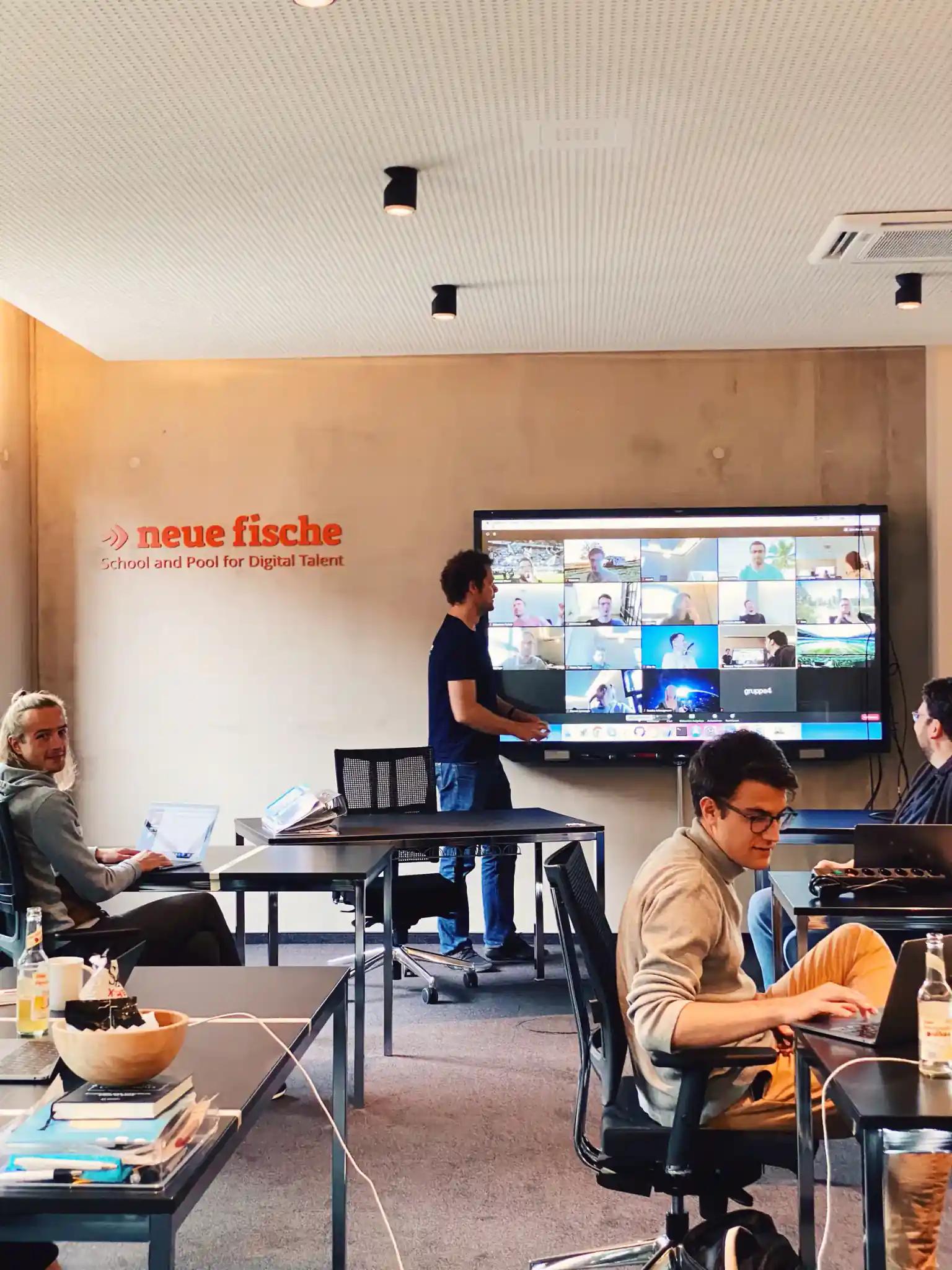 Modern training room with people and online meeting on screen.