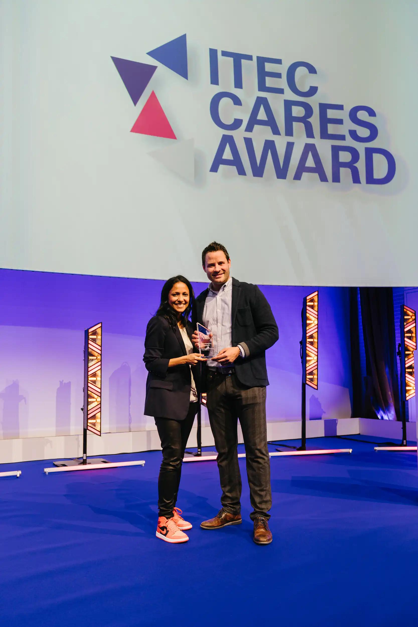 Two people holding an award on stage at the ITEC Cares Award event.