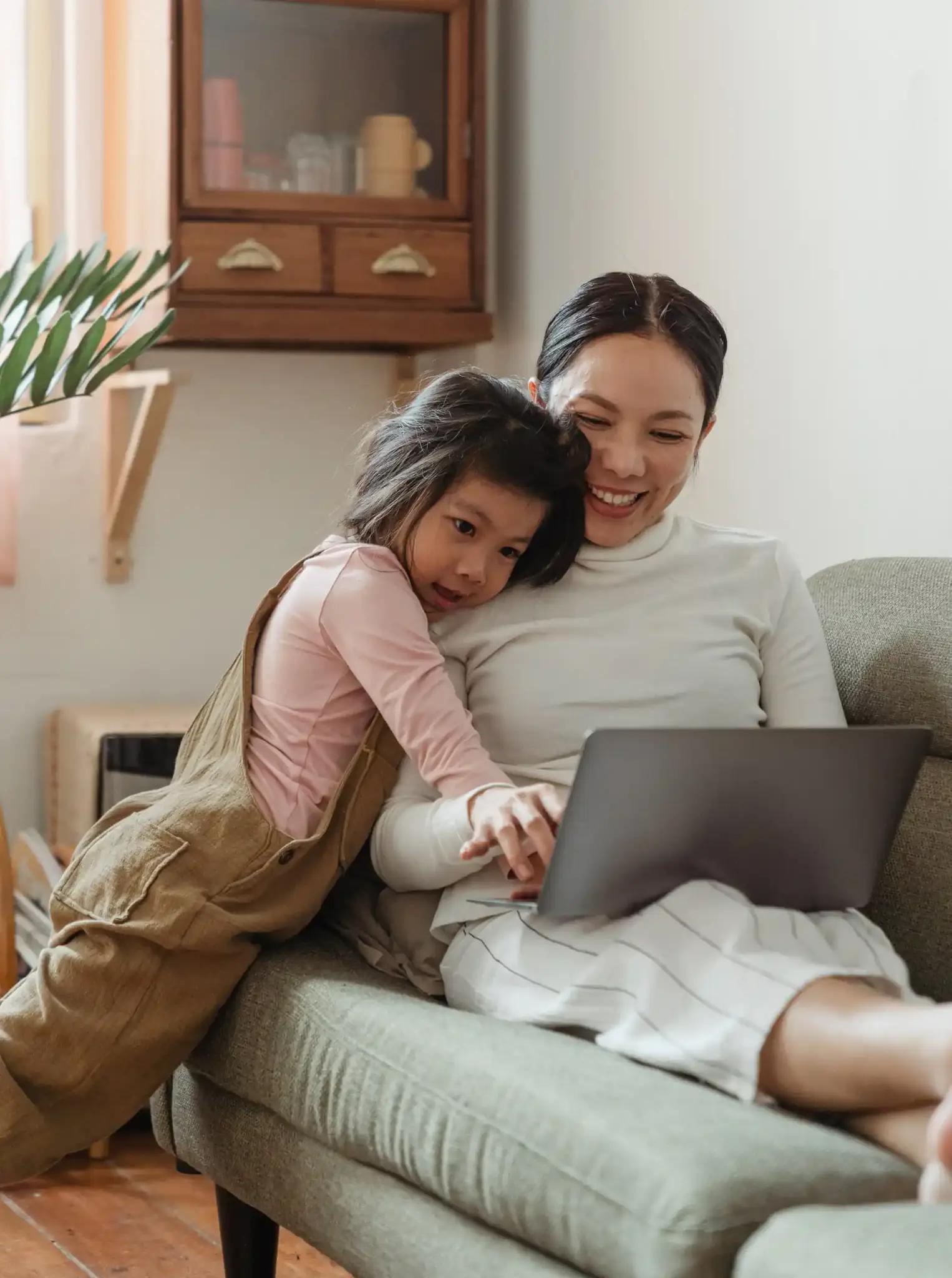 Mother and daughter using laptop together on sofa.