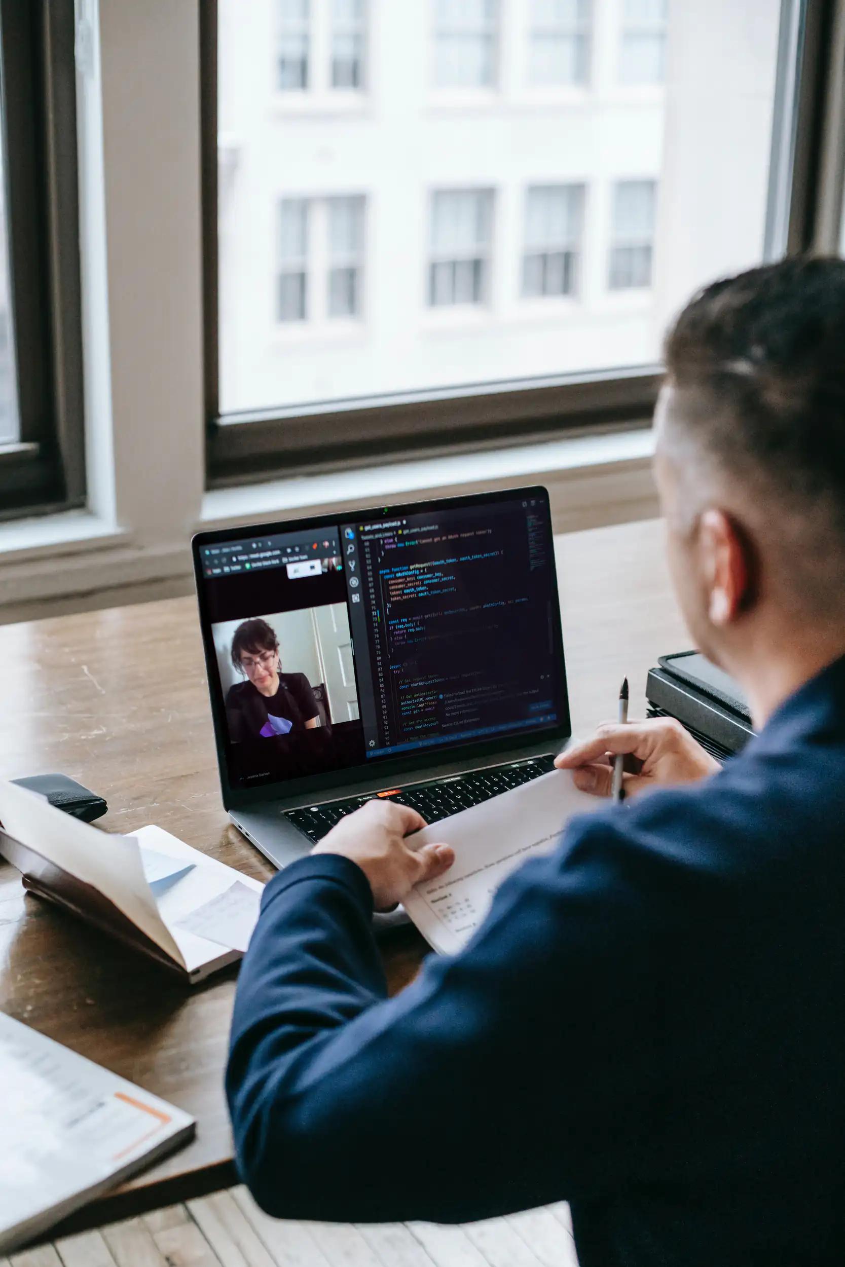 Person arbeitet am Laptop mit Videokonferenz und Programmiercode