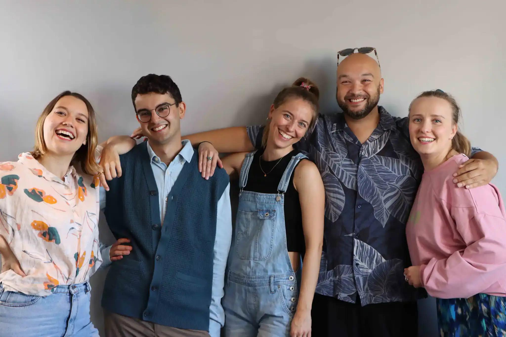Group of five happy friends posing in front of a wall.
